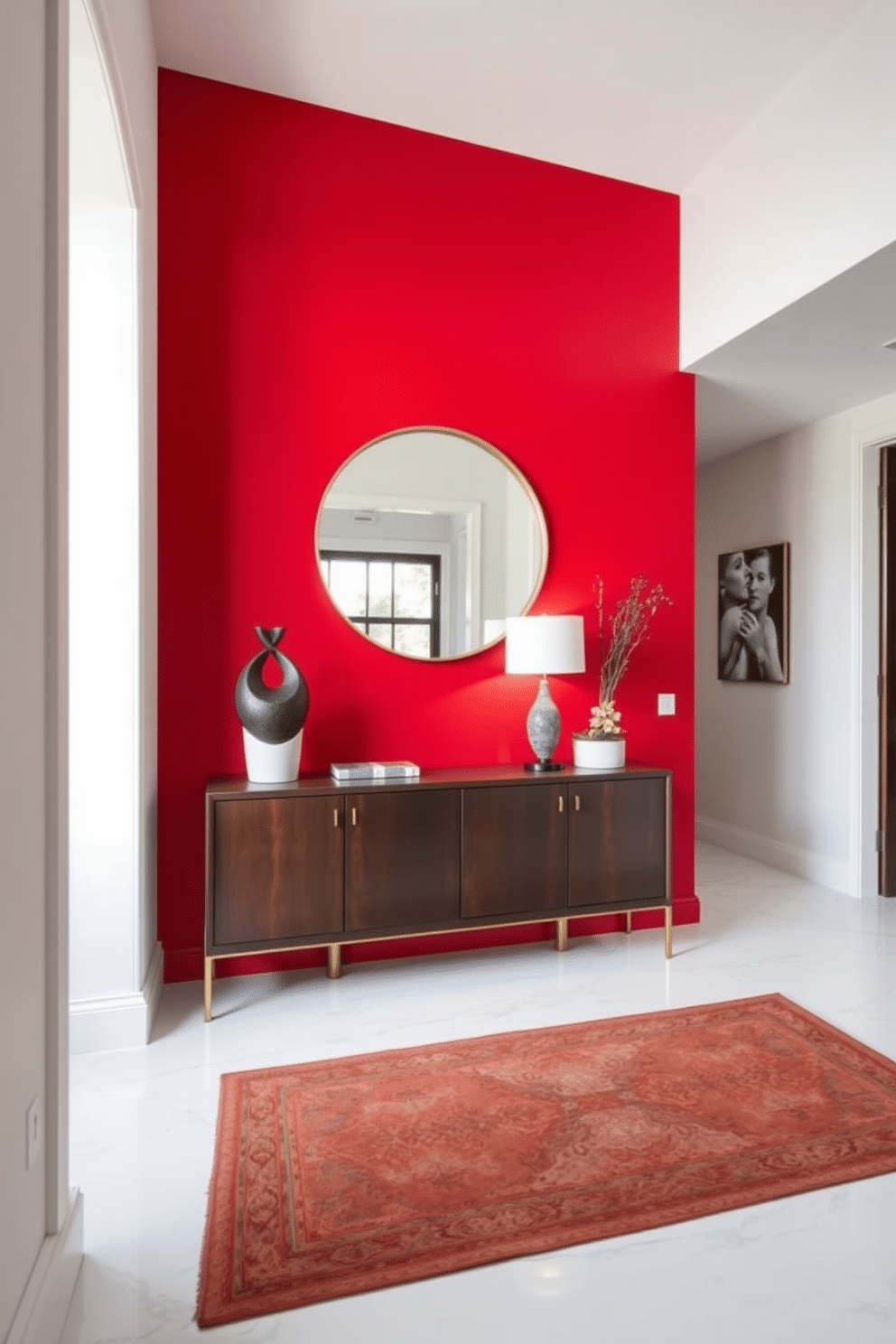 A bold red accent wall serves as the focal point of the foyer, creating a vibrant and inviting atmosphere. Complementing the striking wall, a sleek console table in a dark wood finish is adorned with a modern sculpture and a stylish lamp. The floor features a polished white marble that contrasts beautifully with the red, enhancing the overall elegance of the space. A large round mirror with a thin gold frame hangs above the console, reflecting light and adding depth to the design.