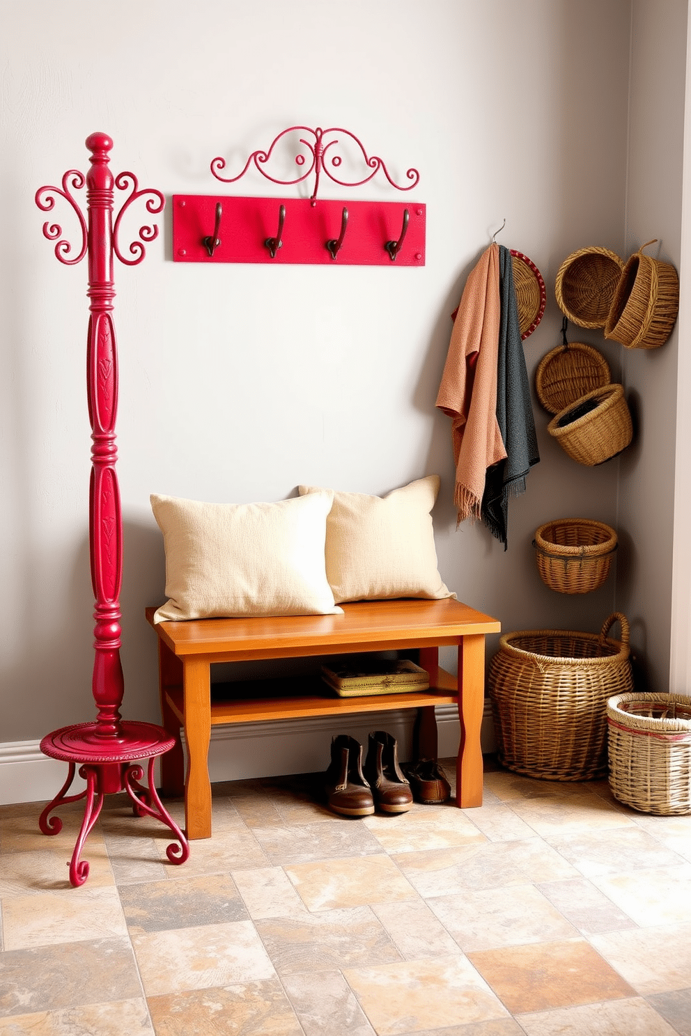 A charming red coat rack stands against a soft gray wall, showcasing its vintage appeal with intricate detailing and a distressed finish. The mudroom features a warm wood bench below the coat rack, adorned with plush cushions in coordinating colors, inviting comfort and style. The floor is laid with rustic, patterned tiles that blend earthy tones, creating an inviting atmosphere. To the side, a collection of woven baskets provides stylish storage for shoes and outdoor gear, enhancing the room's functionality and aesthetic.