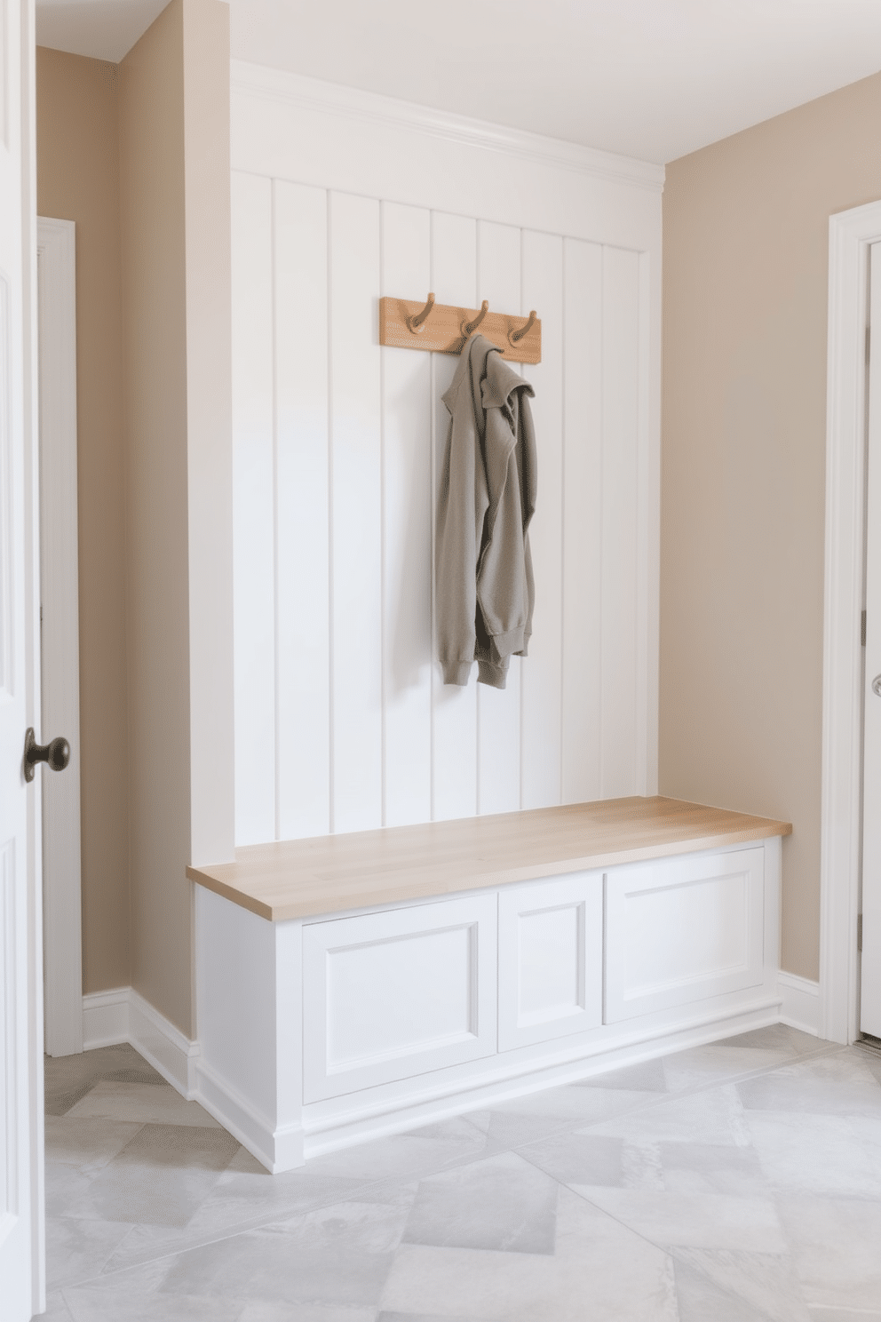 A serene mudroom featuring a neutral palette to create a calming effect. The walls are painted in soft beige, complemented by white shiplap accents and a light wood bench with built-in storage underneath. A stylish coat rack made of natural wood is mounted on the wall, providing a functional yet aesthetic touch. The floor is adorned with large, textured tiles in a light gray hue, enhancing the overall tranquility of the space.