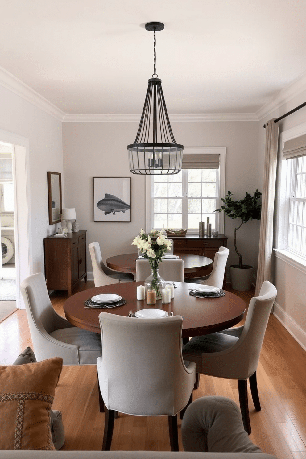 A cozy small dining room featuring an open layout with minimal barriers, allowing for seamless flow between spaces. The room is adorned with a round wooden table surrounded by upholstered chairs, and large windows let in natural light, enhancing the inviting atmosphere. Soft, neutral tones dominate the walls and decor, complemented by a statement pendant light hanging above the table. A small sideboard against one wall provides additional storage and display space for elegant dinnerware and decorative accents.