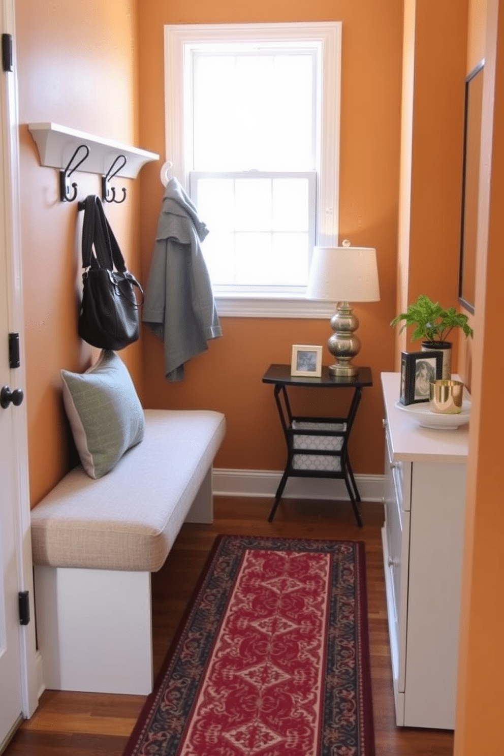 A cozy entryway features a cushioned bench upholstered in a soft, textured fabric, providing both comfort and style. Flanking the bench are decorative hooks for coats and bags, set against a warm, inviting wall color that enhances the space's charm. The floor is adorned with a stylish runner that adds a pop of color and pattern, while a small console table sits nearby, topped with a chic lamp and a few curated decor pieces. Natural light filters in through a nearby window, creating an airy and welcoming atmosphere.