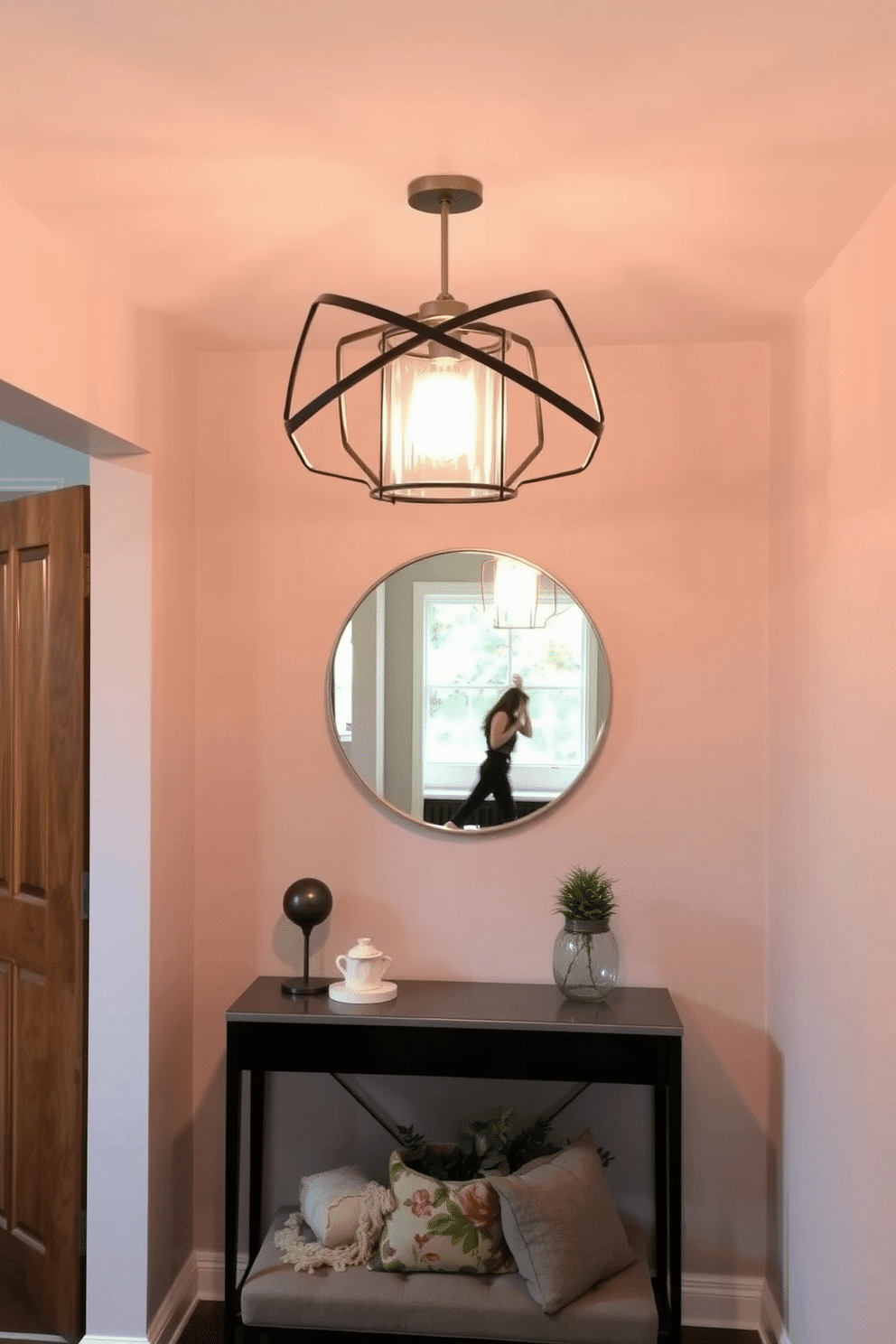 A striking statement light fixture hangs from the ceiling, casting a warm glow over the small foyer. The walls are painted in a soft, welcoming hue, complemented by a stylish console table adorned with decorative accents. A round mirror with a sleek frame reflects the light fixture, enhancing the sense of space. A cozy bench with plush cushions provides a functional yet inviting touch, while a small potted plant adds a pop of greenery to the design.