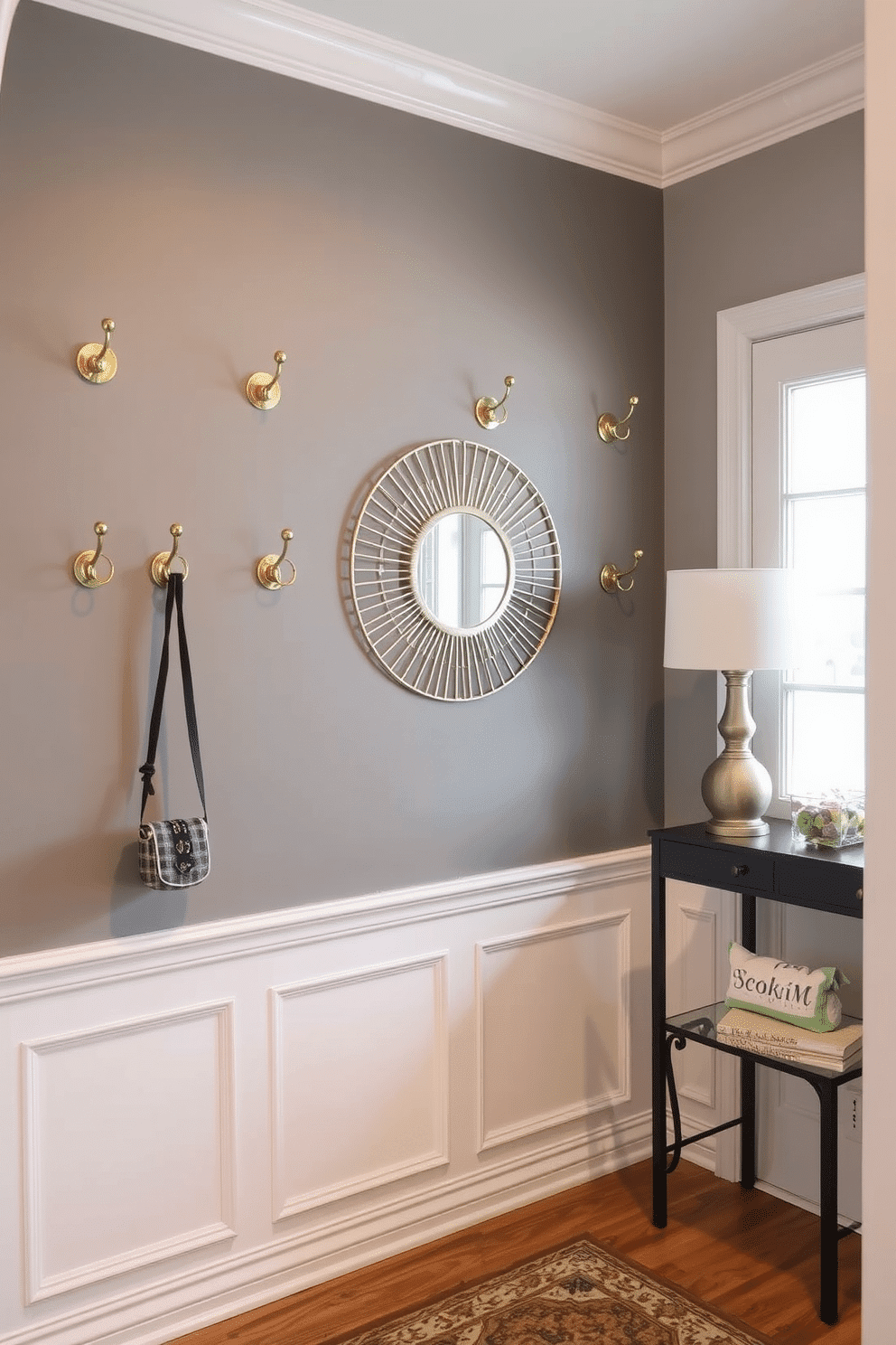 A cozy foyer featuring wall-mounted coat hooks made of brushed brass, elegantly arranged to provide easy access and organization. The walls are painted in a soft, warm gray, complemented by a small console table with a decorative mirror above it, creating an inviting entrance.