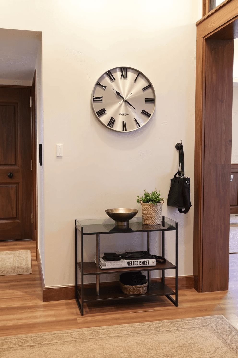 A stylish wall clock is mounted on the wall, featuring a sleek design with a minimalist aesthetic and a brushed metal finish. Below the clock, a small console table is adorned with a decorative bowl and a potted plant, creating an inviting focal point in the foyer. The foyer is designed with a combination of warm wood tones and soft lighting, enhancing the welcoming atmosphere. A stylish area rug anchors the space, while wall hooks provide practical storage for coats and bags, keeping the area organized and functional.