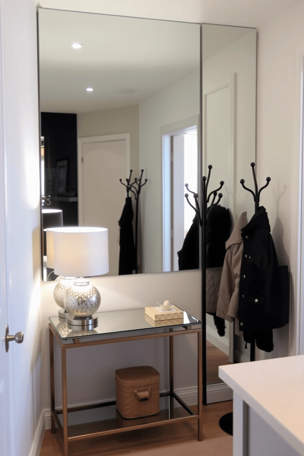 A small foyer featuring a mirrored accent wall that reflects light and creates an illusion of depth. The space includes a sleek console table with a decorative lamp and a stylish coat rack, all set against soft, neutral tones.