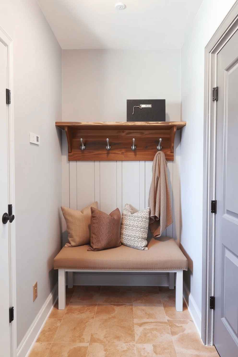 A functional mudroom featuring a stylish hooks and shelves combo, designed for maximum efficiency. The walls are painted in a light gray, and the flooring consists of durable, easy-to-clean tiles in a warm beige tone. The hooks are crafted from brushed nickel, providing a modern touch, while the shelves above are made of reclaimed wood, adding warmth and character. Beneath the shelves, a cushioned bench invites comfort, adorned with decorative pillows in muted earth tones.