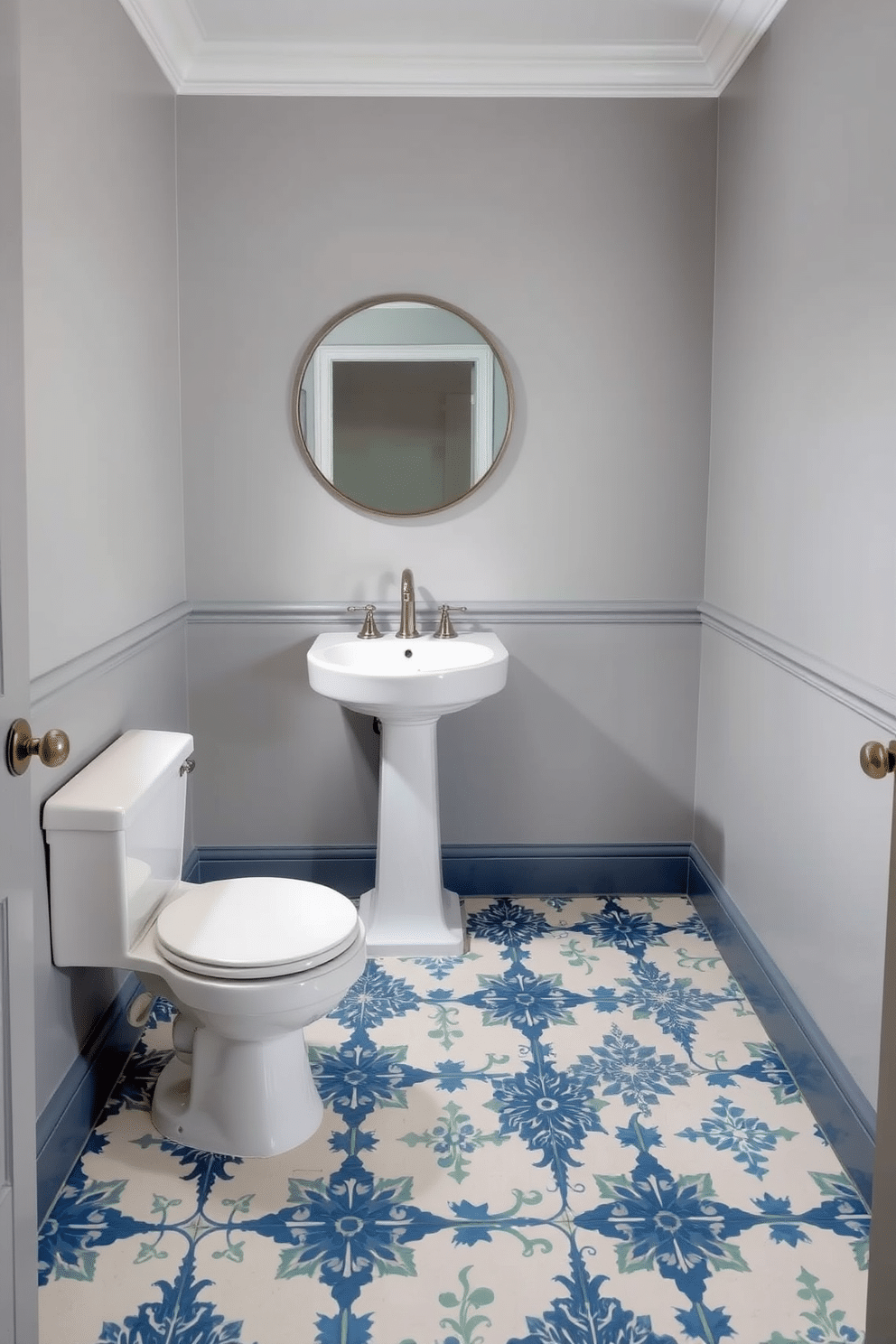 A small powder room features an elegant floor with intricate tile patterns in shades of blue and white, creating a fresh and inviting atmosphere. The walls are adorned with soft gray paint, and a sleek pedestal sink is complemented by a modern round mirror above it.