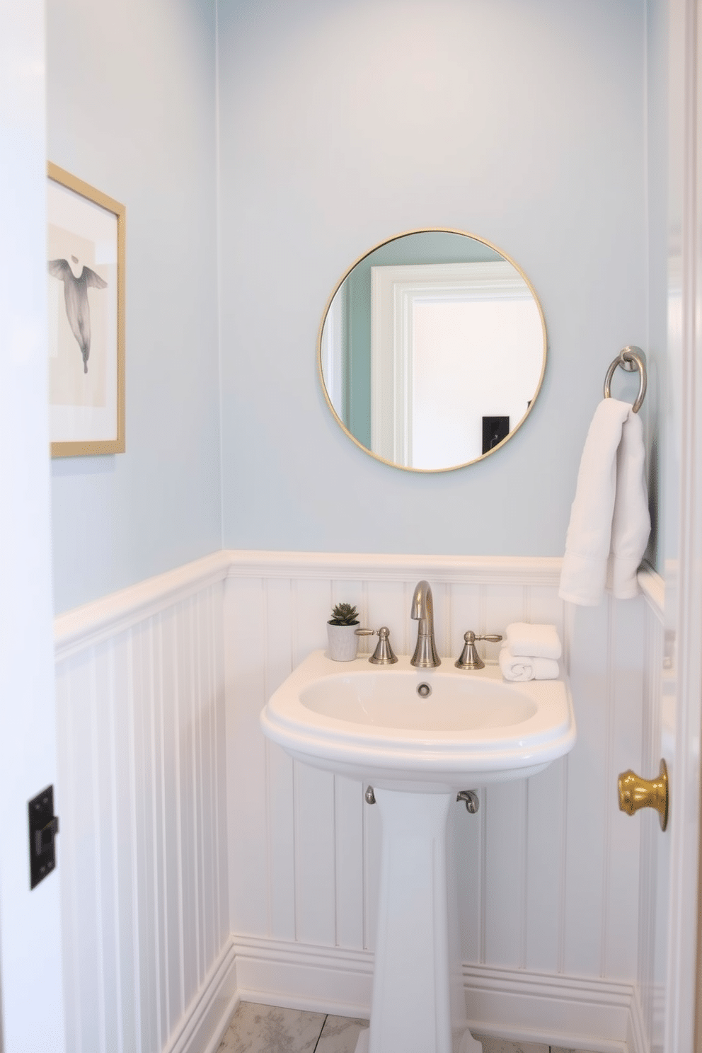 A small powder room features a cohesive color scheme that harmonizes soft blues and crisp whites, creating an airy and inviting atmosphere. The walls are painted in a pale blue hue, while the white wainscoting adds a classic touch, complemented by a stylish white pedestal sink. A round mirror with a thin gold frame hangs above the sink, reflecting the elegant design elements. Decorative accents, such as a small potted plant and neatly folded white towels, are strategically placed to enhance the room's charm without overcrowding the limited space.