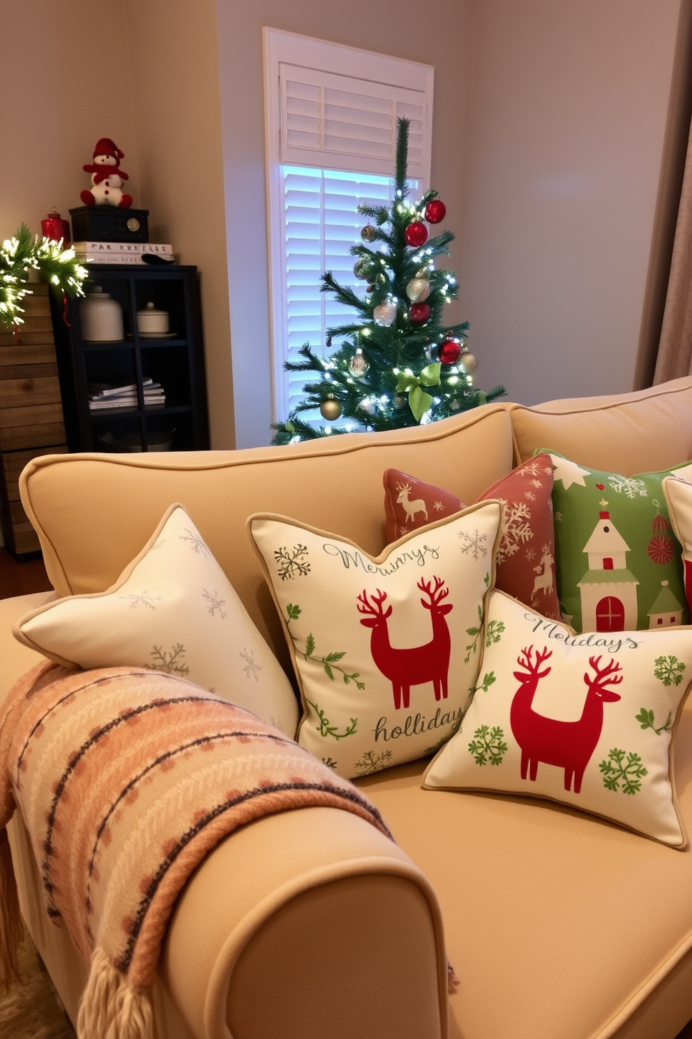 A cozy living room adorned with seasonal throw pillows in festive patterns and colors. The sofa is layered with plush cushions featuring snowflakes, reindeer, and holiday-themed designs, creating a warm and inviting atmosphere. In the corner, a small Christmas tree is decorated with twinkling lights and delicate ornaments, complementing the overall decor. A decorative throw blanket drapes over the arm of the sofa, adding texture and comfort to the space.