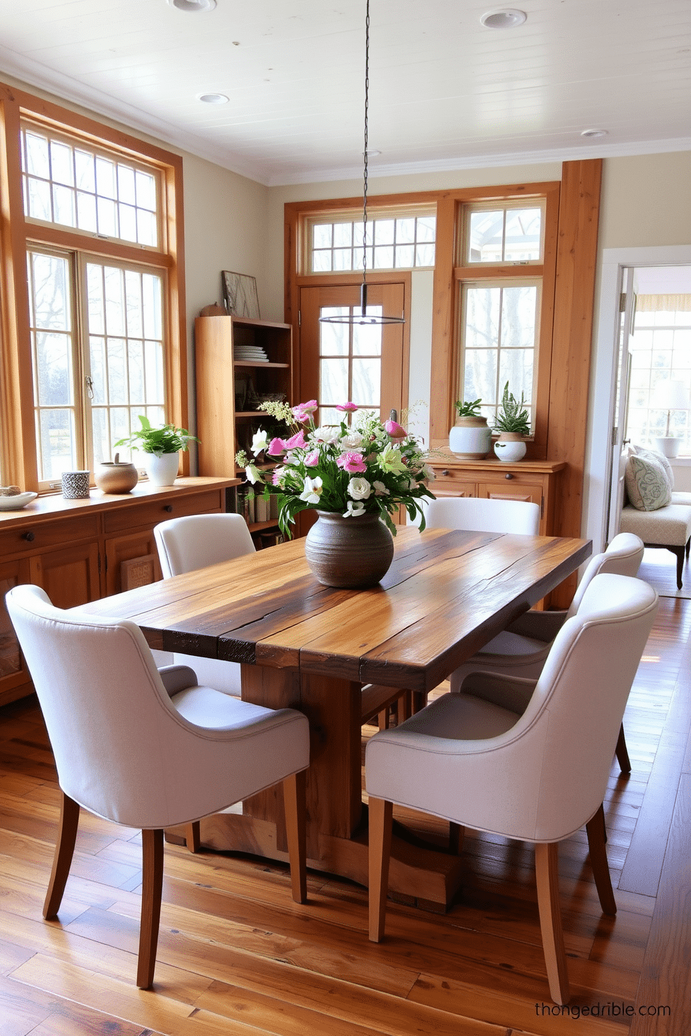 A bright and inviting dining room filled with natural wood elements. The table is made of reclaimed wood and is surrounded by comfortable upholstered chairs in soft pastel colors. Large windows allow sunlight to flood the space, highlighting the warm tones of the wood. A centerpiece of fresh flowers in a rustic vase adds a touch of spring charm to the table.