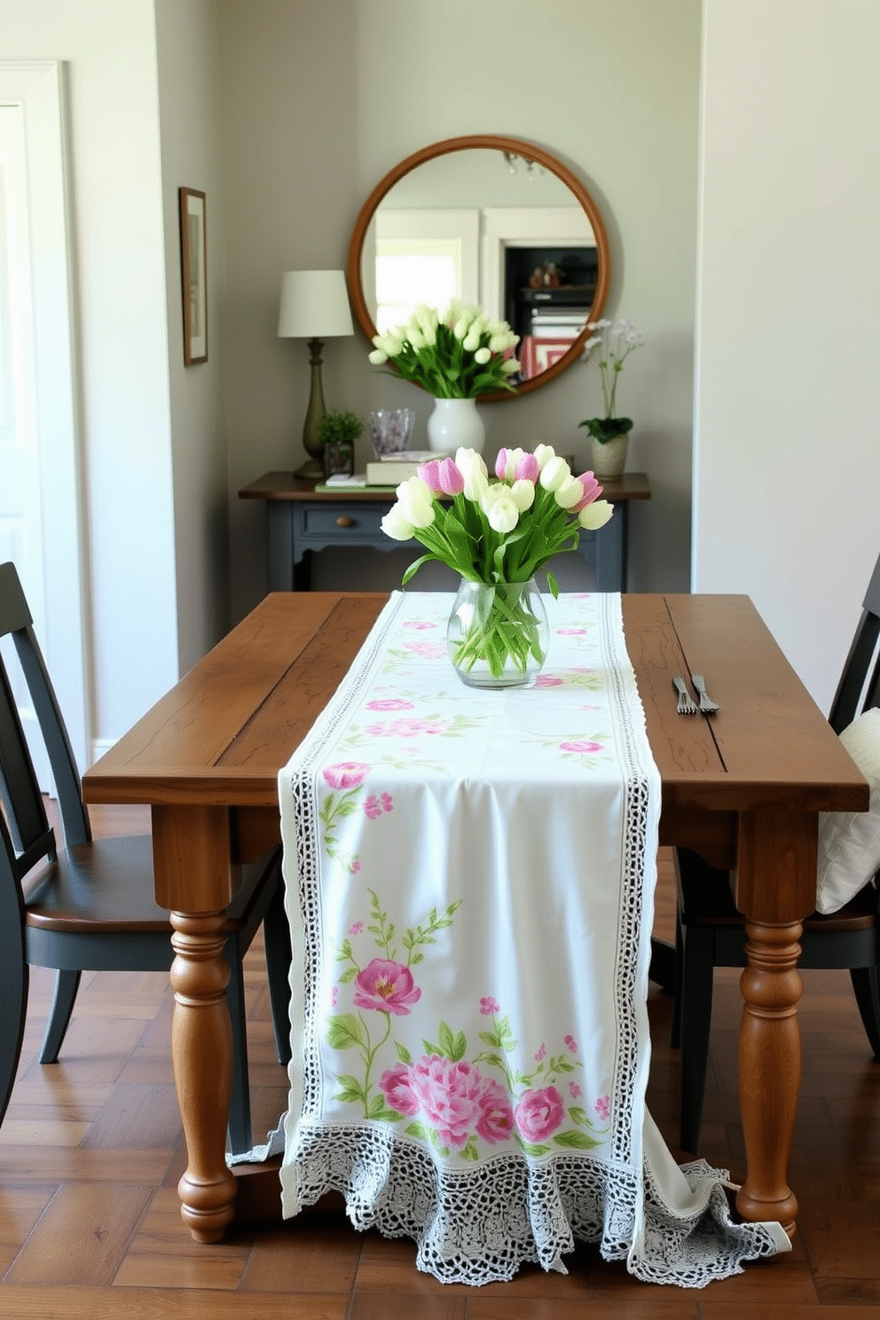 A spring-themed table runner drapes elegantly over a rustic wooden dining table. The runner features vibrant floral patterns in pastel colors, complemented by delicate white lace trim. The entryway is adorned with a charming console table topped with a fresh bouquet of tulips. Soft green accents and a large round mirror create a welcoming atmosphere that captures the essence of spring.