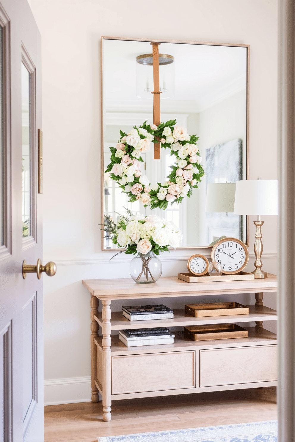 Floral wreath on the front door creates a welcoming atmosphere. The entryway features a soft pastel color palette with light wood accents and a stylish console table. A large mirror hangs above the console, reflecting natural light and enhancing the space. Fresh flowers in a vase and decorative trays add a touch of elegance to the entryway decor.