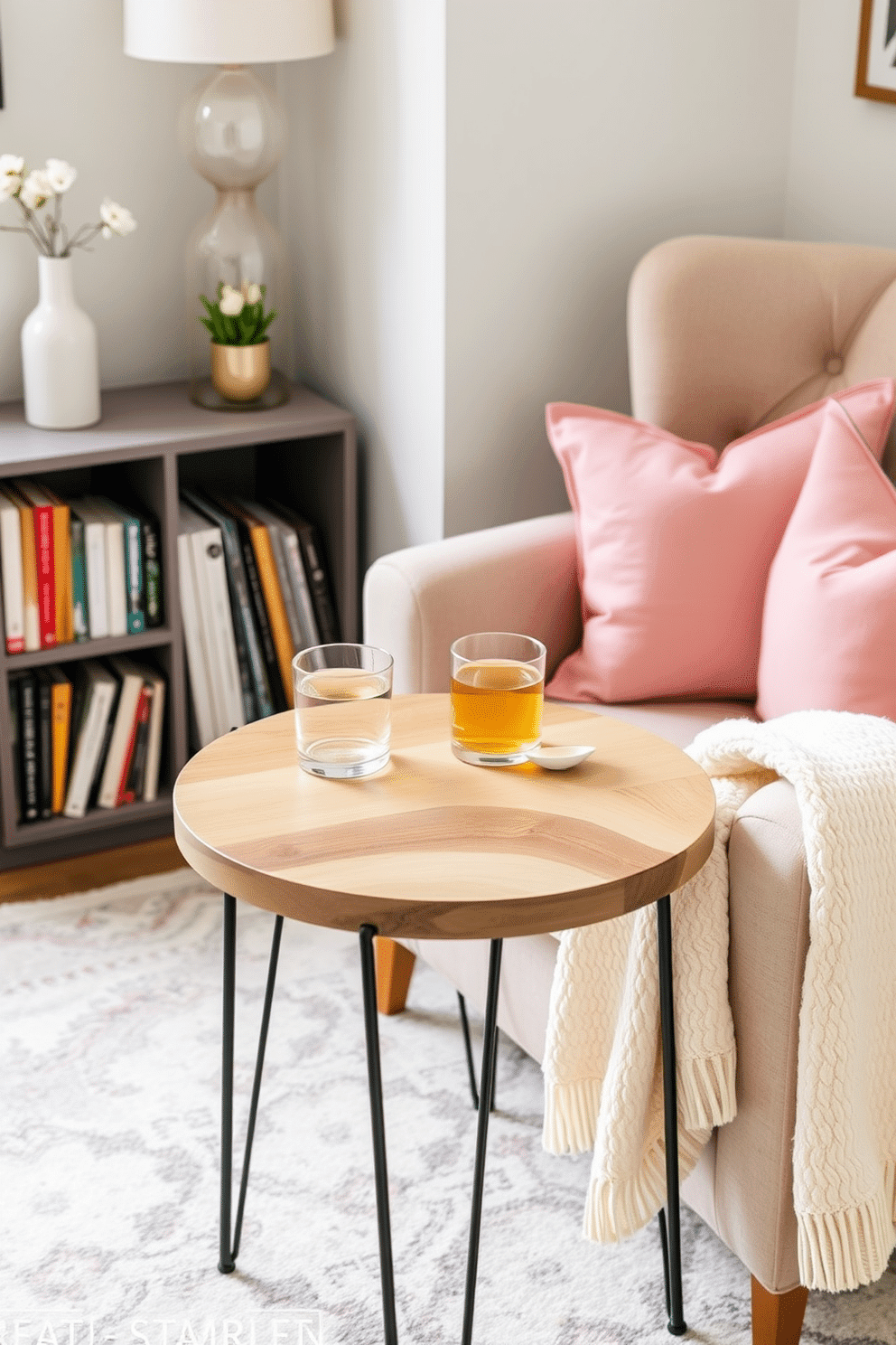 A charming side table designed for drinks and snacks features a round wooden top with a natural finish. It is complemented by slender metal legs that add a touch of elegance and modernity. The spring reading nook is adorned with soft pastel cushions and a cozy throw blanket draped over a plush armchair. Nearby, a small bookshelf holds an array of colorful books, inviting relaxation and enjoyment.