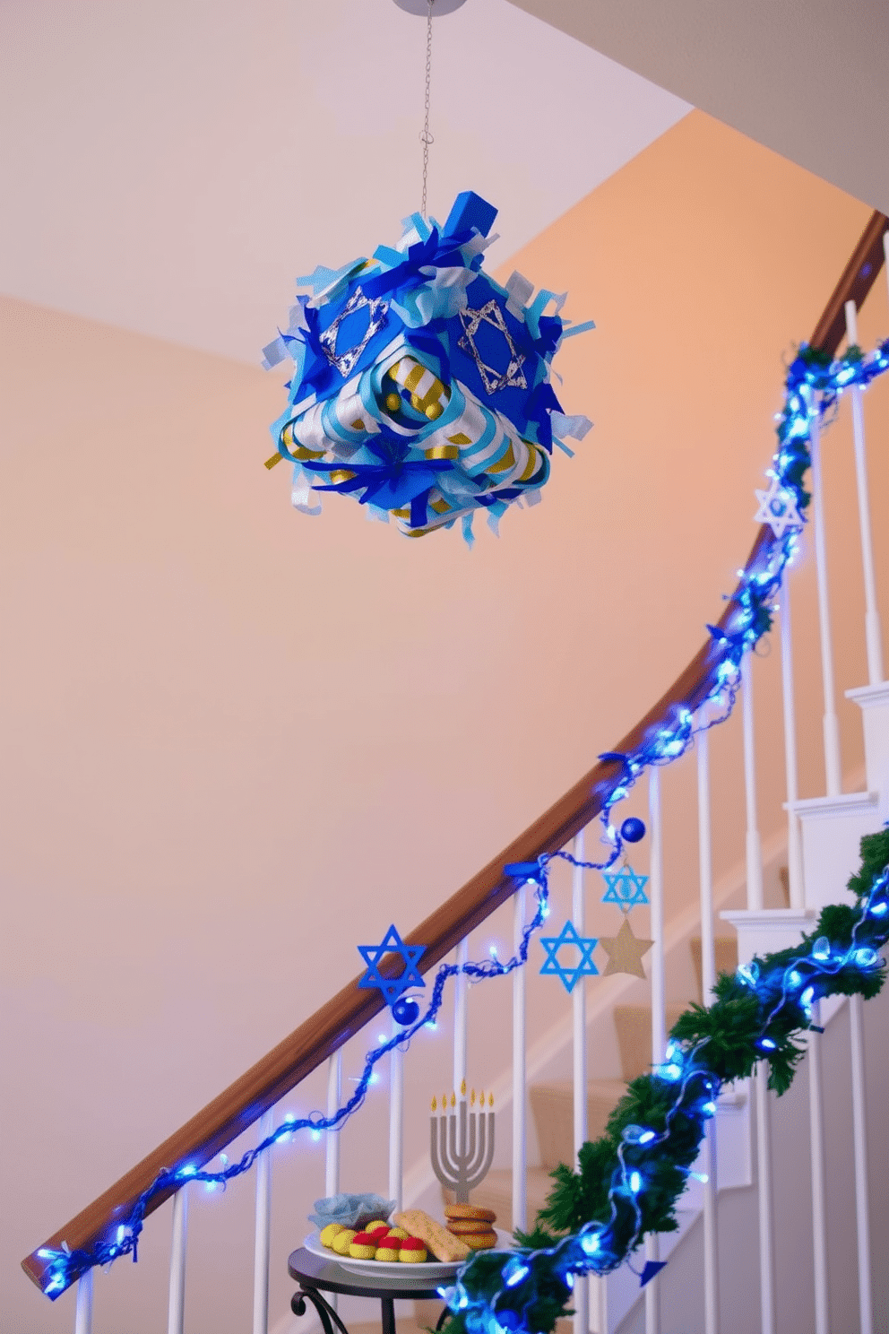 A festive DIY dreidel piñata decoration hangs from the ceiling, crafted from colorful tissue paper in vibrant shades of blue, silver, and gold. Below the piñata, a small table is adorned with traditional Hanukkah treats, including gelt and sufganiyot, creating a cheerful atmosphere. The staircase is elegantly decorated for Hanukkah, with strings of blue and white lights winding along the banister. Handmade ornaments featuring stars of David and menorahs dangle from the railing, adding a touch of warmth and celebration to the home.