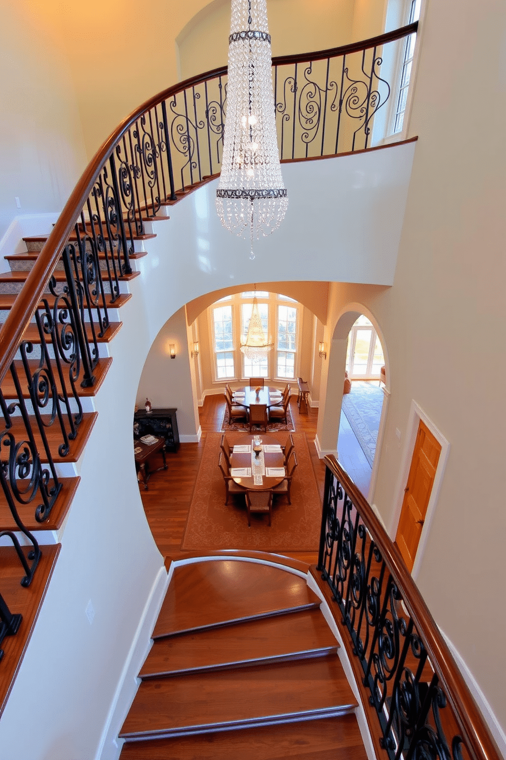 An elegant staircase gracefully curves upward, adorned with a stunning crystal chandelier that casts a warm glow over the space. The staircase features rich wooden steps and a polished banister, complemented by intricate wrought iron railings. In the dining room, the staircase creates a dramatic focal point, leading to an open space filled with natural light. The dining area is elegantly furnished with a long, polished table surrounded by upholstered chairs, enhancing the sophisticated atmosphere.