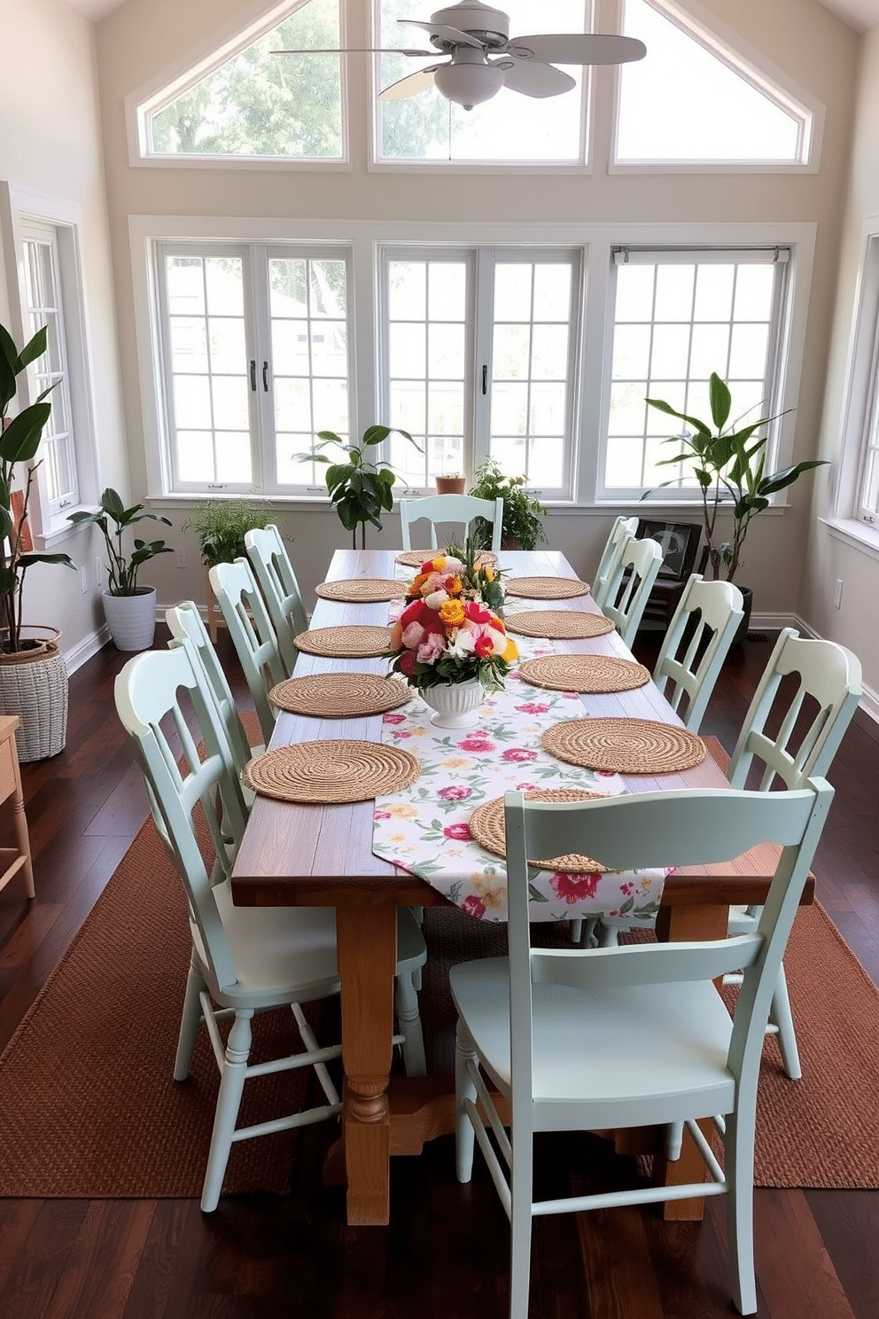 Lightweight chairs arranged around a long wooden dining table create a casual and inviting atmosphere. The chairs are painted in soft pastel colors, complementing the vibrant floral tablecloth and seasonal centerpieces. Large windows allow natural light to flood the space, enhancing the cheerful ambiance. Potted plants in the corners add a touch of greenery, while woven placemats provide texture and warmth to the table setting.