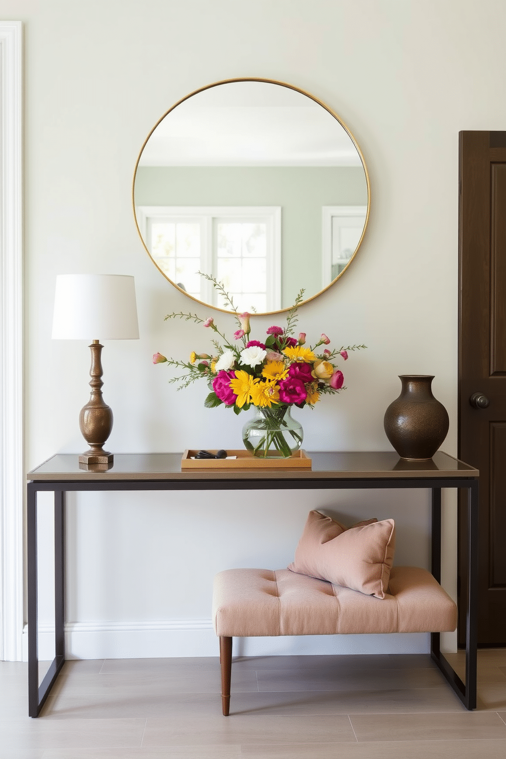 A stylish entryway featuring a sleek console table against a soft pastel wall. The table is adorned with a vibrant bouquet of seasonal flowers and a decorative tray holding keys and small essentials. To the side, a cozy bench with plush cushions invites guests to sit. A large round mirror above the console reflects natural light, enhancing the airy feel of the space.