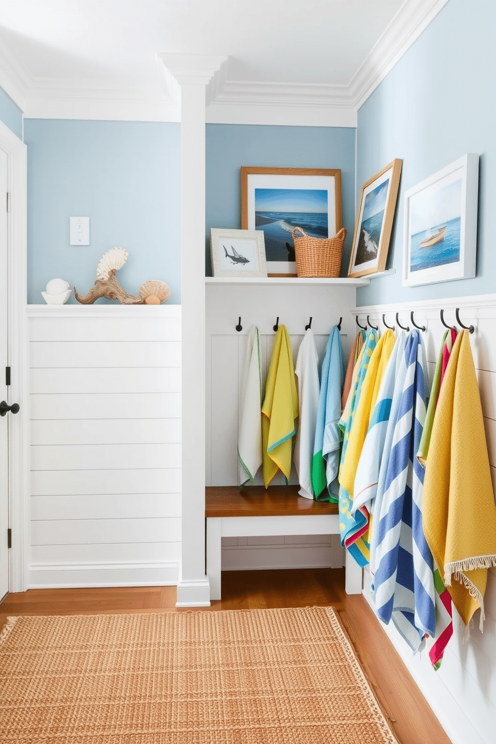 A bright and airy mudroom features a charming coastal theme. Light blue walls complement white shiplap accents, while a woven seagrass rug adds warmth underfoot. Beach-themed accessories are displayed on open shelving, including seashells, driftwood, and framed ocean prints. A collection of colorful beach towels hangs neatly on hooks, inviting a fun and relaxed vibe.