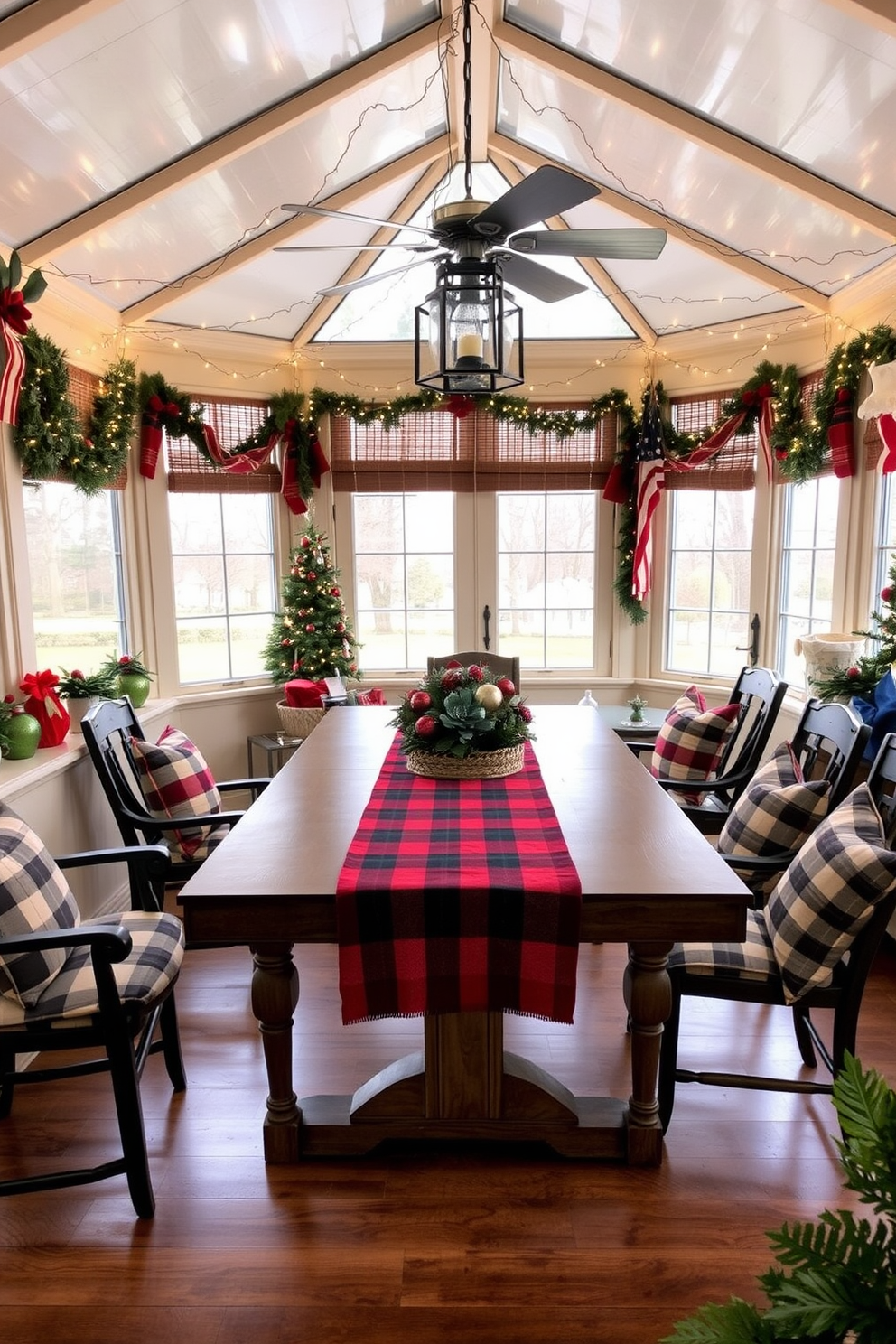 A cozy sunroom adorned for Christmas features a large, inviting table in the center, draped with a festive red and green table runner that complements the seasonal decor. Surrounding the table, comfortable chairs are decorated with plaid cushions, and twinkling fairy lights hang from the ceiling, creating a warm and cheerful atmosphere.