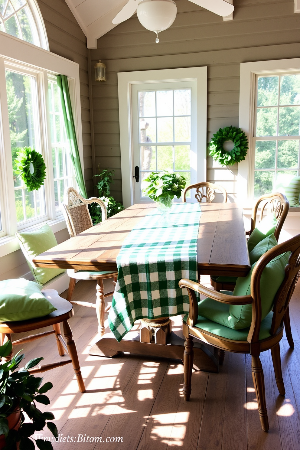 A sunlit sunroom features a green and white checkered tablecloth draped elegantly over a rustic wooden dining table. Surrounding the table are mismatched vintage chairs, each adorned with soft cushions in various shades of green, creating a cozy and inviting atmosphere for St. Patrick's Day celebrations.