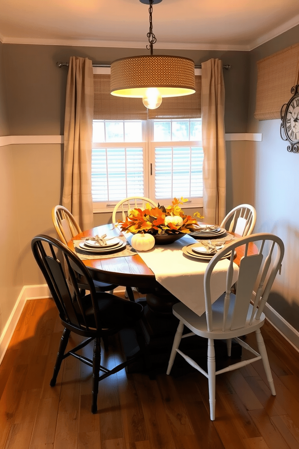 A cozy dining area designed for Thanksgiving celebrations. The space features a rustic wooden table adorned with a white tablecloth and a centerpiece of autumn leaves and pumpkins. Surrounding the table are mismatched chairs that add charm to the small space. Soft golden lighting from a pendant fixture above enhances the warm, inviting atmosphere.