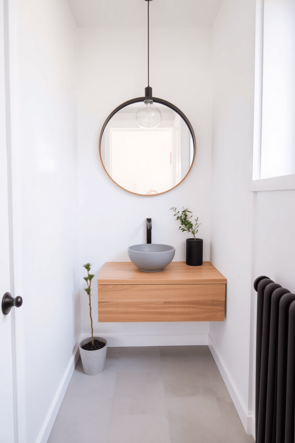 A tiny powder room with minimalist decor emphasizes simplicity and functionality. The walls are painted in a soft white, creating an airy feel, while a sleek floating vanity with a small round sink features a natural wood finish. A large round mirror hangs above the vanity, reflecting the light from a stylish pendant fixture. The floor is adorned with light gray tiles, and a single potted plant adds a touch of greenery without overwhelming the space.