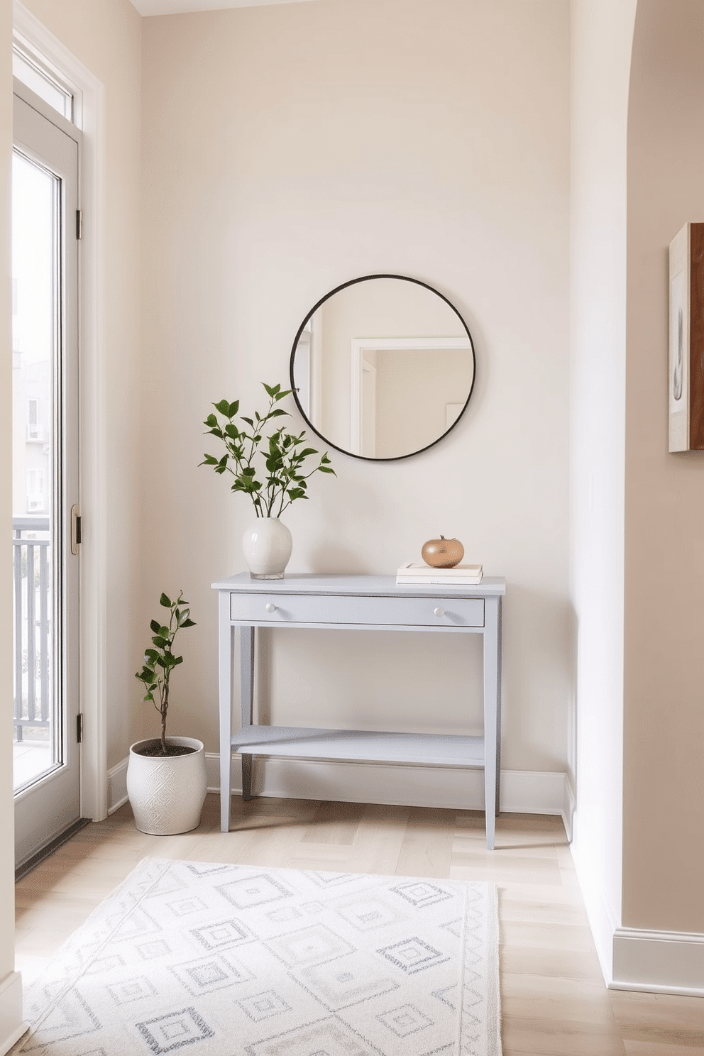 A serene townhouse entryway features soft beige walls complemented by a light gray console table. Above the table, a round mirror with a thin black frame reflects natural light, enhancing the airy feel of the space. The floor is adorned with a subtle patterned rug in muted tones, providing warmth and texture. A potted plant in the corner adds a touch of greenery, while minimalist artwork hangs on the walls, creating an inviting atmosphere.