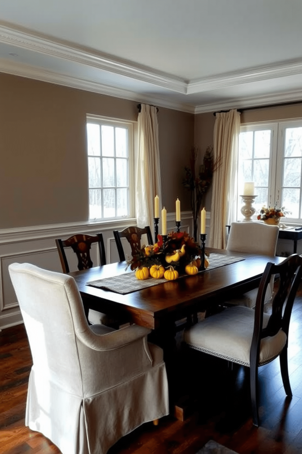 A cozy dining room adorned with seasonal decor that reflects the warmth of autumn. A centerpiece of vibrant gourds and candles is placed on a rustic wooden table, surrounded by plush chairs in earthy tones. The walls are painted a soft taupe, complemented by elegant wainscoting that adds depth to the space. Large windows draped with sheer, flowing curtains allow natural light to illuminate the room, enhancing the inviting atmosphere.