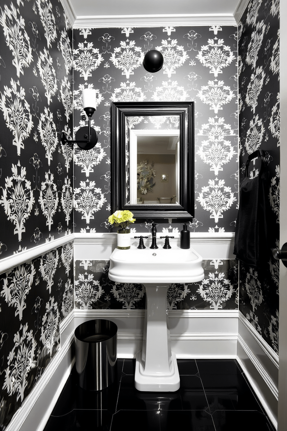 A chic powder room designed in a striking black and white theme. The walls are adorned with bold black wallpaper featuring intricate white patterns, while the floor boasts glossy black tiles that reflect the light. A sleek pedestal sink with a white finish takes center stage, complemented by a stylish black framed mirror above it. Elegant black accents, such as a vintage sconce and decorative accessories, enhance the classic elegance of the space.