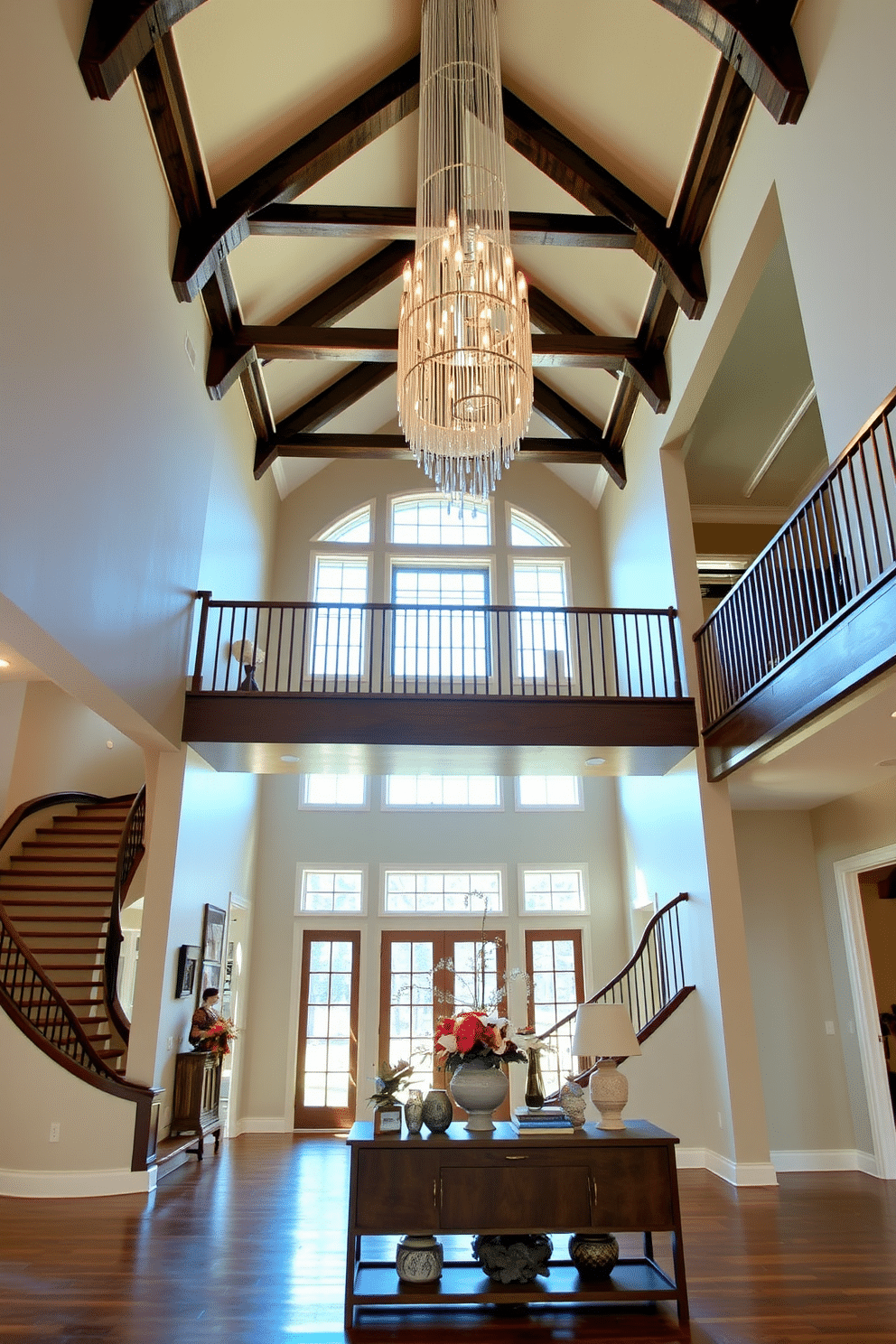 A grand two-story foyer welcomes guests with its soaring ceilings and architectural beams that add a rustic charm. The space is illuminated by a stunning chandelier that cascades down, highlighting the rich wood accents and an inviting staircase that curves gracefully upward. Natural light floods in through large windows, creating a warm atmosphere that complements the earthy tones of the decor. A statement console table adorned with fresh flowers and decorative accents anchors the space, inviting visitors to explore further.