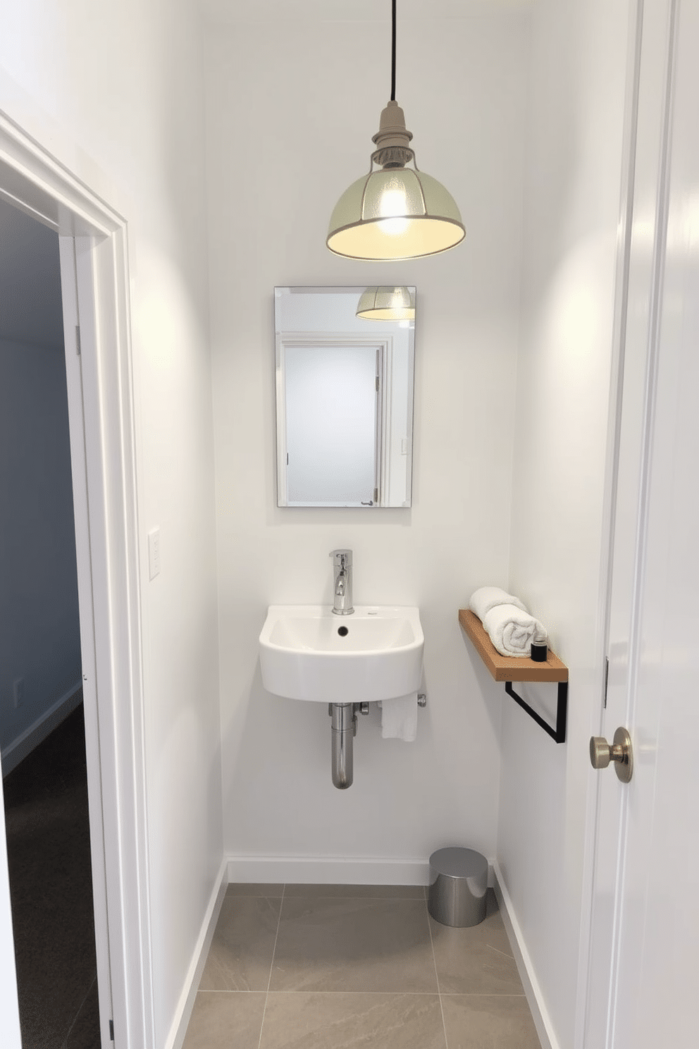 A cozy under-stairs bathroom featuring a compact design with a sleek, wall-mounted sink and a minimalist mirror above. The walls are painted in a soft white, while the floor is adorned with light gray tiles, creating a bright and airy feel. To the side, a small wooden shelf holds neatly rolled towels and essential toiletries. A stylish pendant light hangs from the ceiling, illuminating the space and adding a touch of elegance.