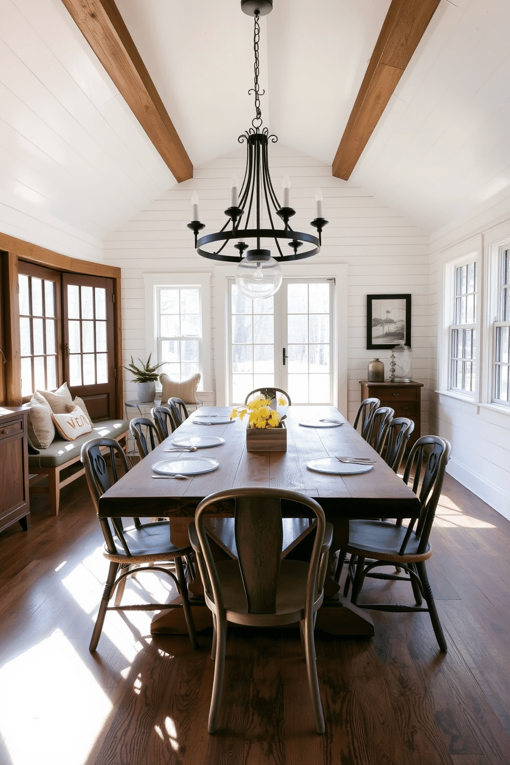 A rustic dining room exuding charm features a large reclaimed wood table at its center, surrounded by mismatched vintage chairs. The walls are adorned with white shiplap, and a statement chandelier made of wrought iron hangs above, casting a warm glow over the space. Natural light floods in through large windows, highlighting the earthy tones of the decor. A cozy nook with a built-in bench, filled with plush cushions, invites family gatherings and intimate dinners.