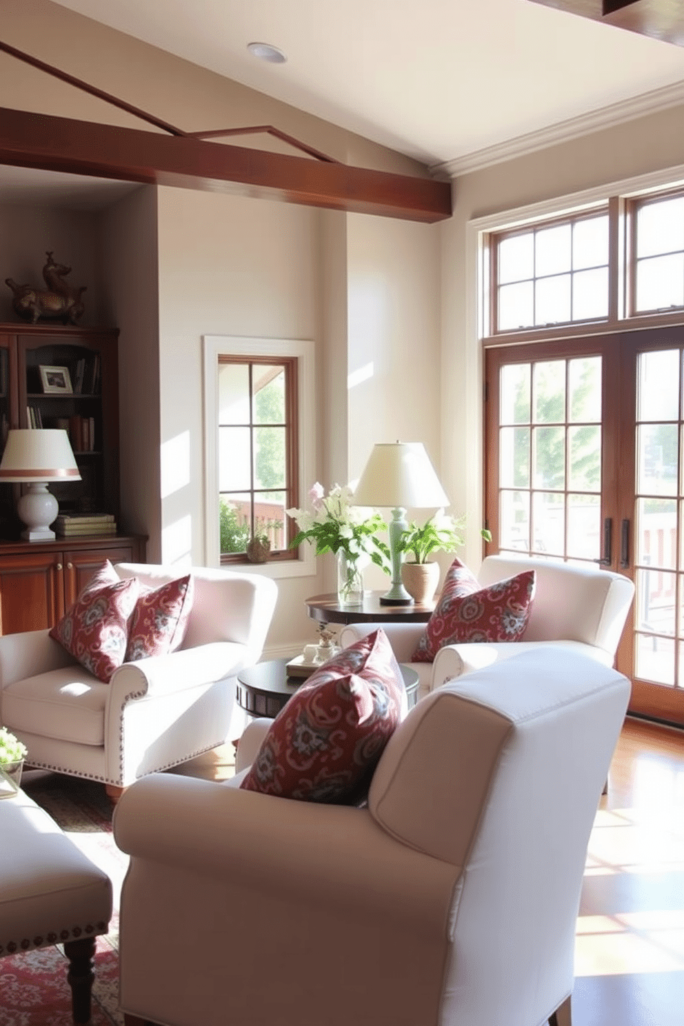 A cozy family room featuring comfortable white armchairs adorned with vibrant patterned pillows. The space is illuminated by natural light streaming through large windows, creating a warm and inviting atmosphere.