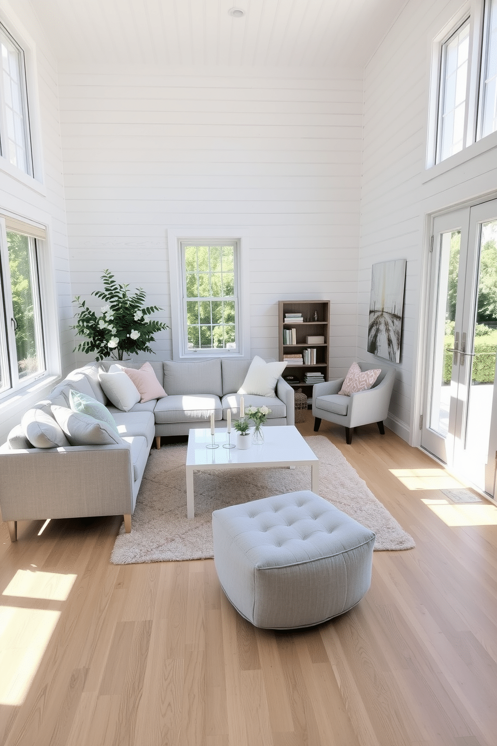 Airy white space with large windows. The room features a plush, light grey sectional sofa adorned with pastel throw pillows, facing a sleek white coffee table. Natural light floods the space, highlighting the white shiplap walls and light oak flooring. A cozy reading nook with a soft armchair and a small bookshelf is nestled in one corner, creating a perfect spot for relaxation.