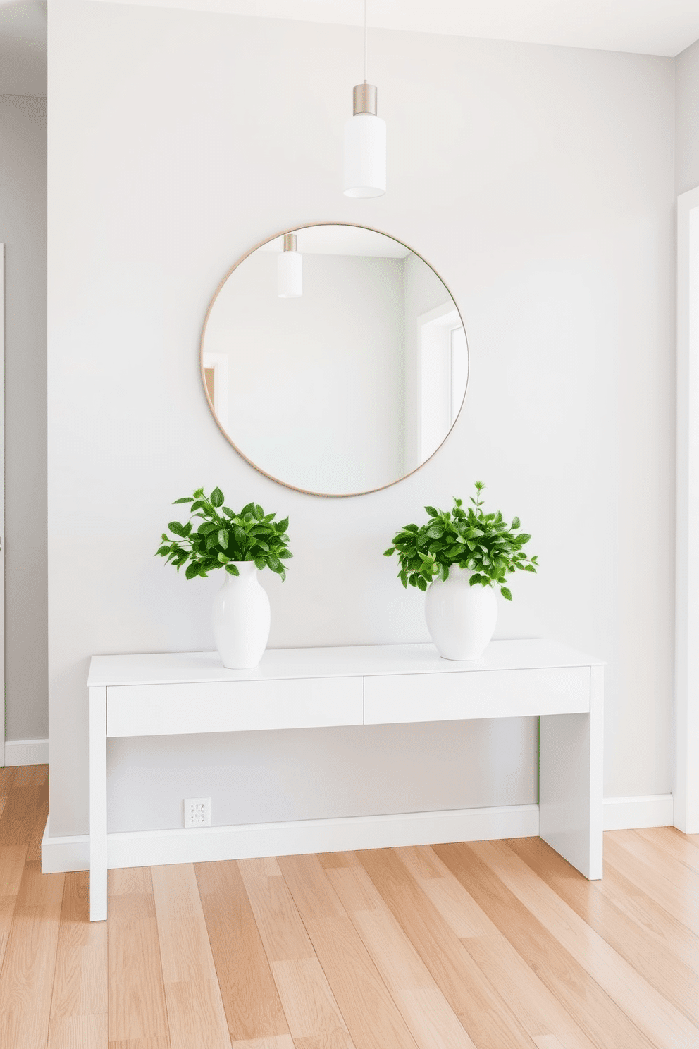 A bright foyer featuring a sleek white console table against a soft gray wall. Above the table, a large round mirror reflects natural light, and on the table, two elegant white ceramic vases filled with lush greenery add a fresh touch. The flooring is a polished light wood, creating warmth and contrast with the white elements. A minimalist pendant light hangs from the ceiling, illuminating the space and enhancing the welcoming atmosphere.