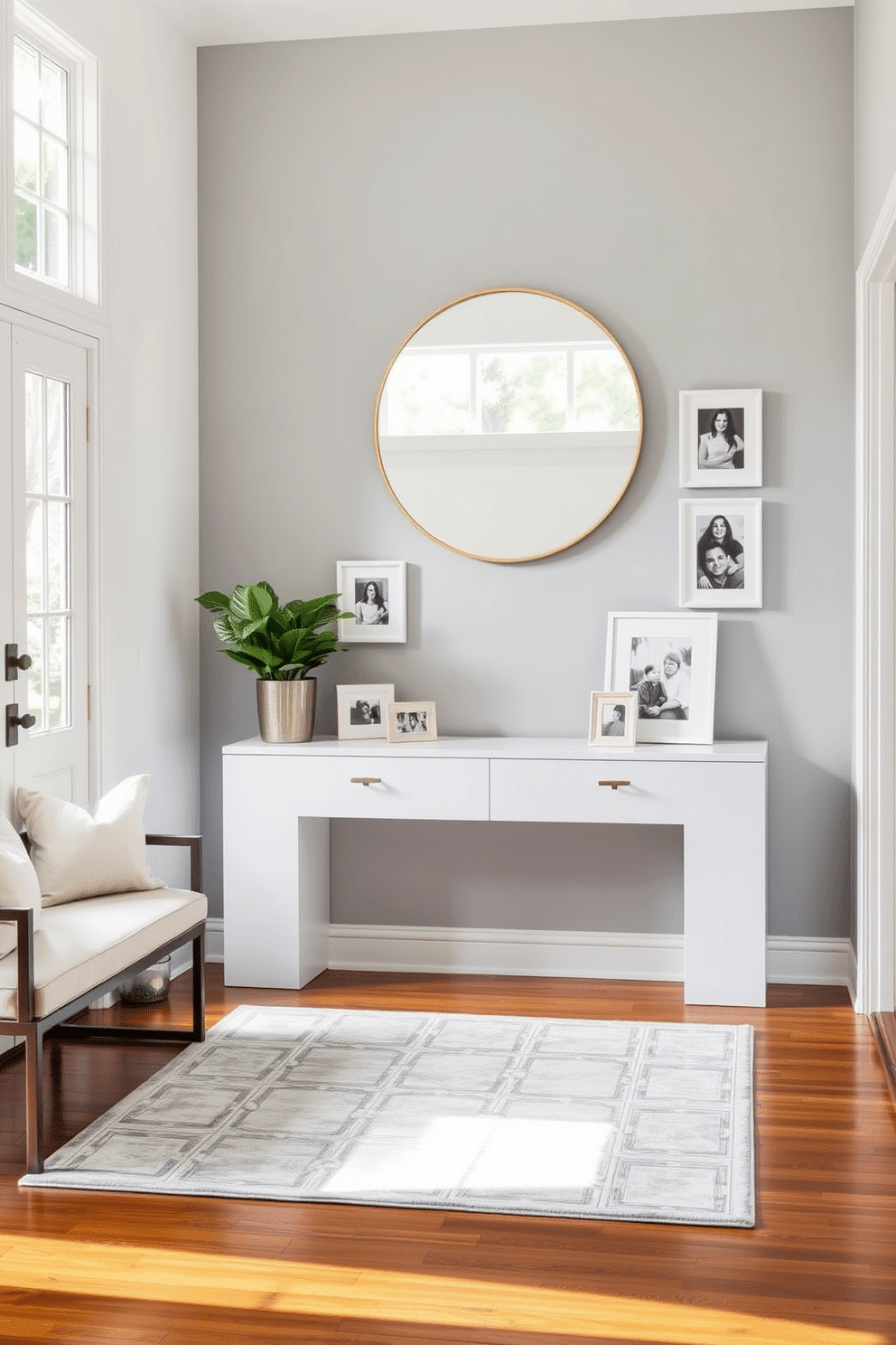 A bright foyer features a sleek console table against a soft gray wall, adorned with framed family photos in white frames that add a personal touch. A large round mirror hangs above the table, reflecting natural light from the nearby window, while a stylish area rug anchors the space with subtle patterns. To the left, a chic bench with plush cushions invites guests to sit, and a potted plant in the corner brings a touch of greenery. The flooring is a polished hardwood, enhancing the inviting atmosphere of this elegant foyer design.