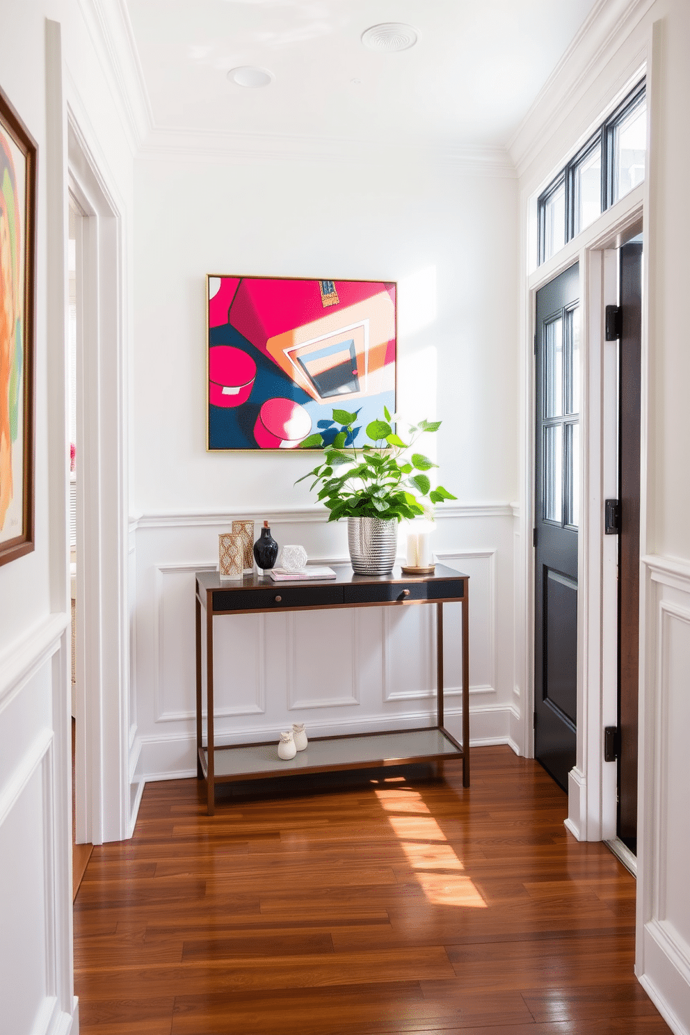 A bright foyer featuring elegant white wainscoting that adds a touch of sophistication to the space. Bold, colorful artwork adorns the walls, creating a striking contrast and serving as a focal point in the entryway. Natural light floods in through a large window, illuminating a stylish console table adorned with decorative objects and a lush green plant. The floor is finished with rich hardwood, complementing the overall design while enhancing the warm and inviting atmosphere.