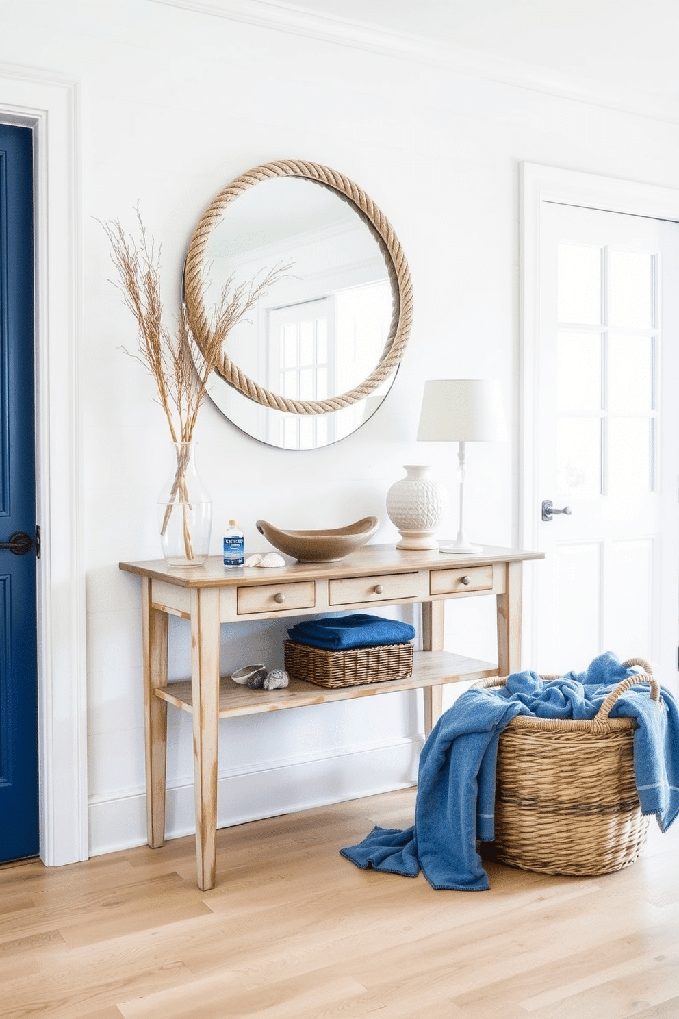 A nautical-themed foyer features crisp white walls adorned with blue accents, evoking a fresh seaside atmosphere. A stylish console table in a weathered finish is placed against the wall, topped with a decorative bowl and a few seashells for added charm. The flooring is a light-colored wood that complements the coastal vibe, while a large round mirror with a rope frame hangs above the console table. To enhance the theme, a woven basket filled with soft blue blankets sits nearby, inviting guests to unwind in this serene entryway.