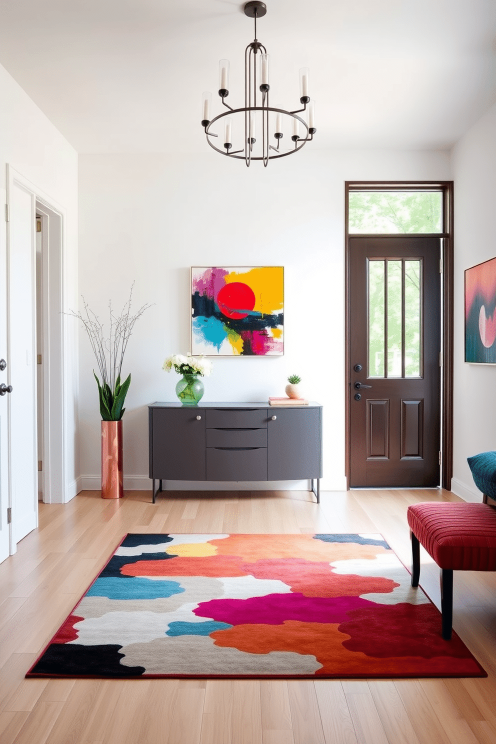 A bright and inviting foyer features a sleek console table against a crisp white wall, adorned with a vibrant abstract painting that adds a splash of color. The floor is laid with light hardwood, and a stylish area rug in bold hues anchors the space, complemented by decorative accents like a colorful vase and fresh flowers. Natural light floods in through a large window, highlighting the cheerful atmosphere of the foyer. A modern chandelier hangs overhead, providing a warm glow that enhances the lively art pieces displayed on the walls.