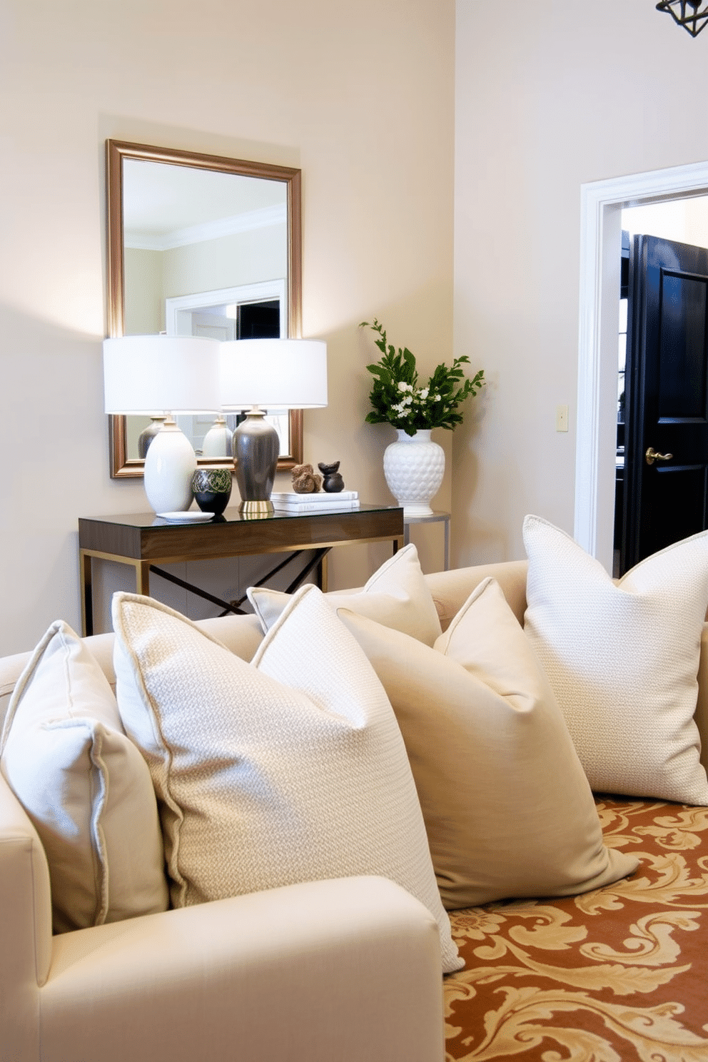 A serene foyer adorned with neutral-toned throw pillows that invite comfort and relaxation. The space features a stylish console table with a sleek lamp, while a large mirror reflects the soft ambient light. The walls are painted in a warm beige, creating a welcoming atmosphere. A beautiful area rug anchors the space, complementing the throw pillows and enhancing the overall design.