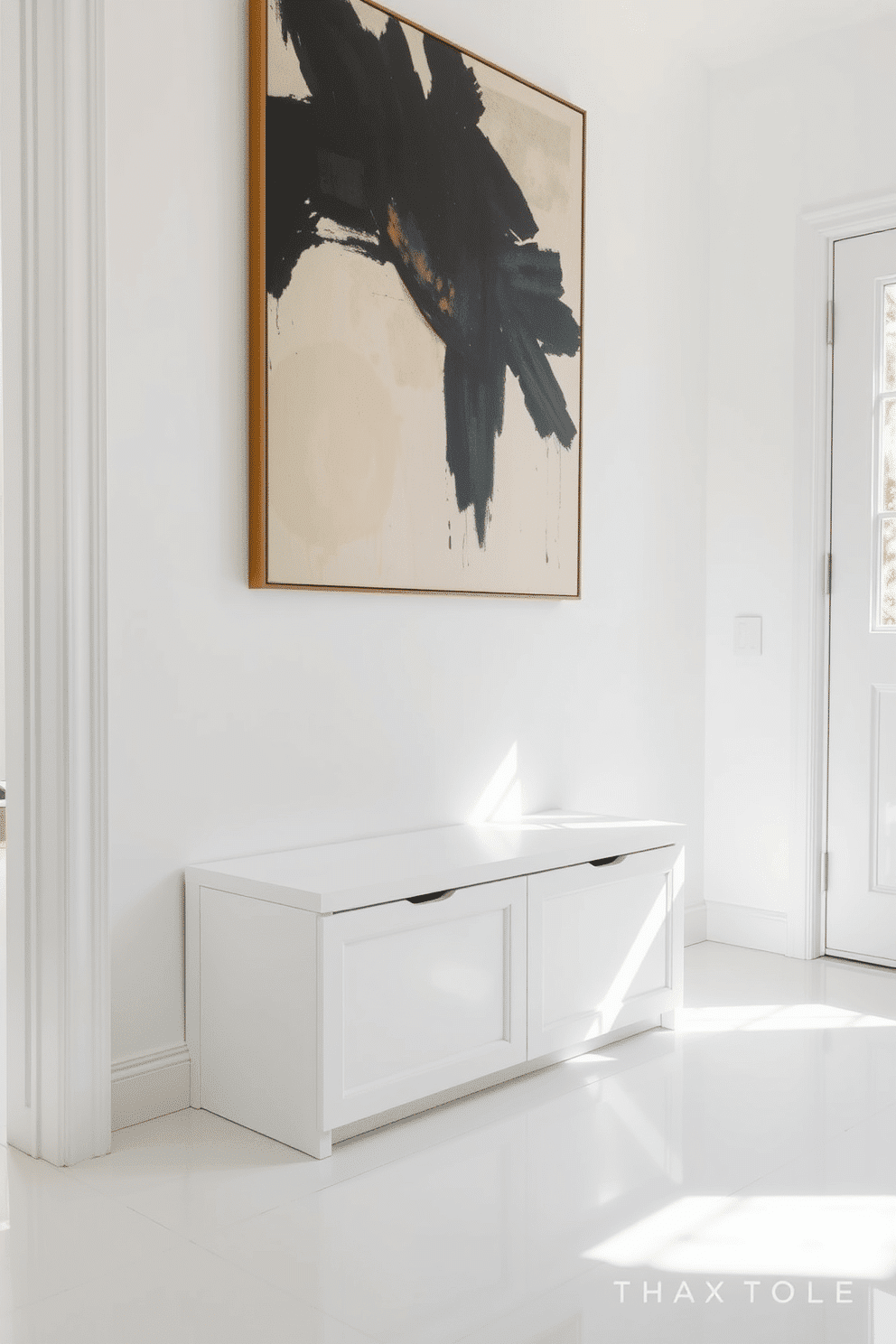 A minimalist bench with hidden storage is positioned against a wall in a bright white foyer. The bench features clean lines and a smooth finish, seamlessly blending into the space while providing practical storage solutions underneath. The foyer is adorned with a large, abstract piece of art above the bench, adding a pop of color to the otherwise neutral palette. Natural light floods in through a nearby window, illuminating the sleek white walls and polished floor, creating an inviting and airy atmosphere.