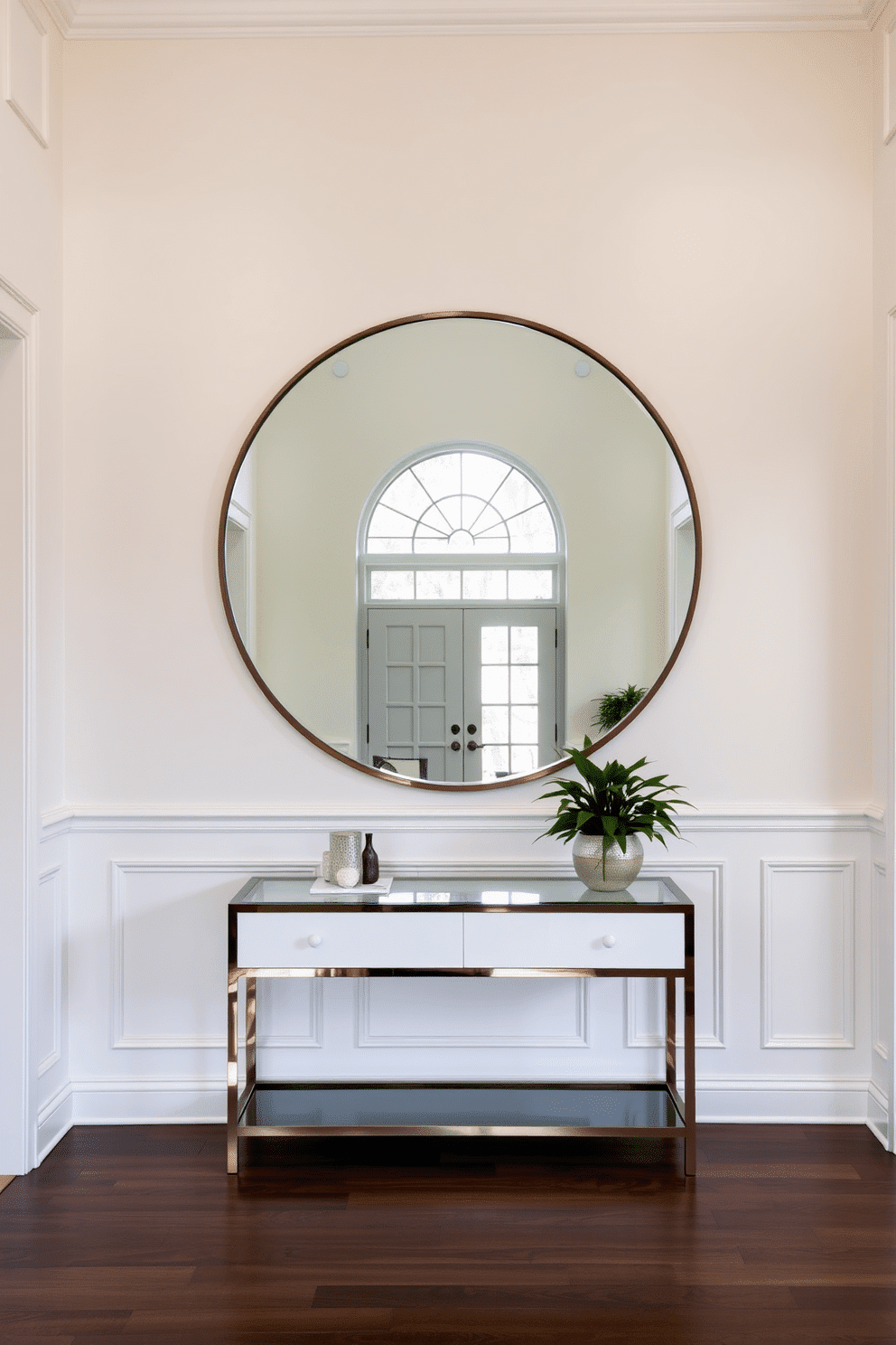 A spacious foyer featuring a large round mirror that reflects natural light, creating an inviting atmosphere. The walls are painted in a soft white, complemented by elegant wainscoting, while a stylish console table sits beneath the mirror, adorned with decorative objects and a small potted plant.