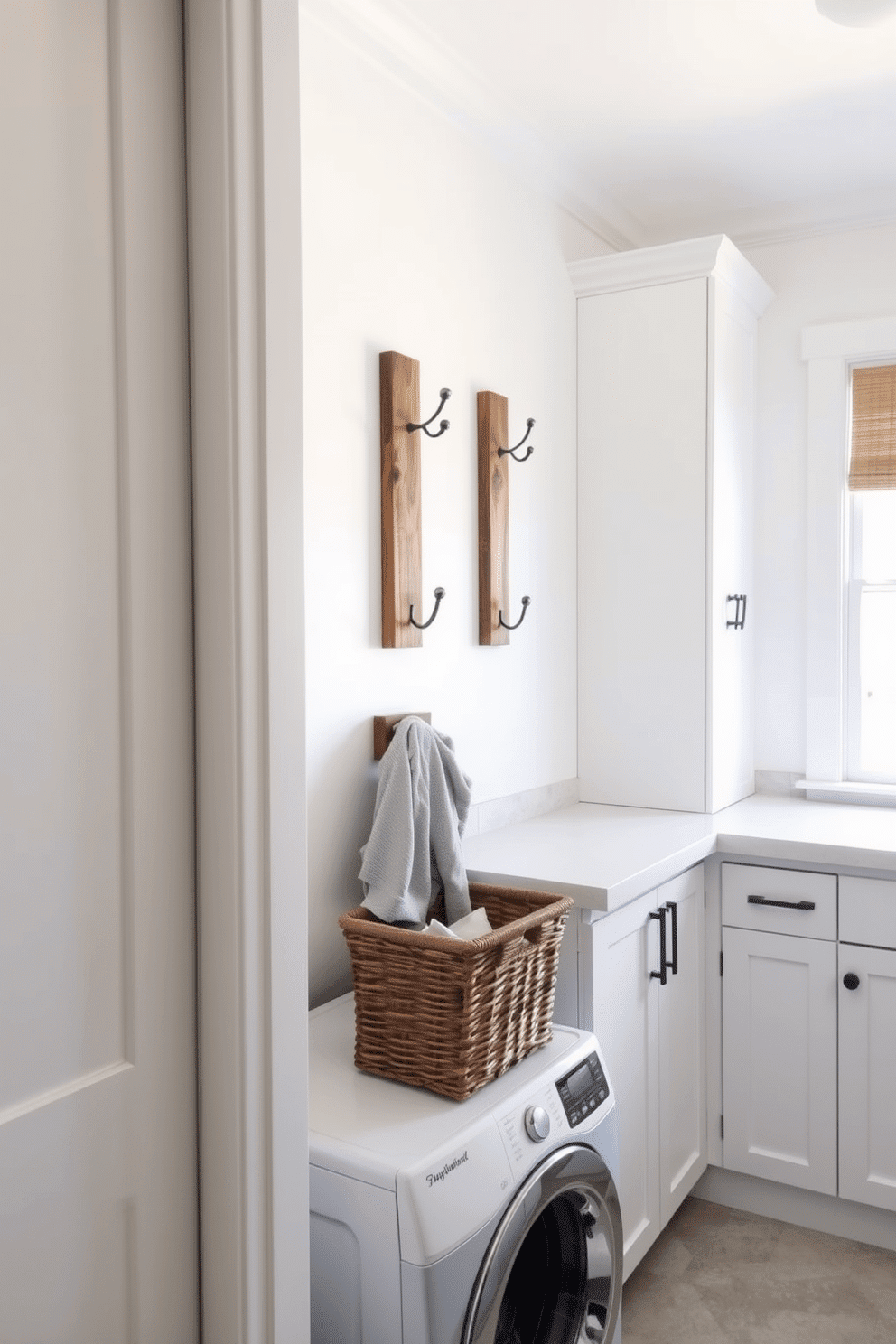 A bright and airy laundry room features decorative wall hooks made from reclaimed wood, adding a touch of rustic charm. The hooks are arranged in a stylish pattern on a soft white wall, providing both functionality and aesthetic appeal. The room is designed with sleek white cabinetry and a spacious countertop for folding clothes, complemented by a large window that lets in natural light. A woven basket sits beneath the hooks, neatly storing laundry essentials while enhancing the overall decor.