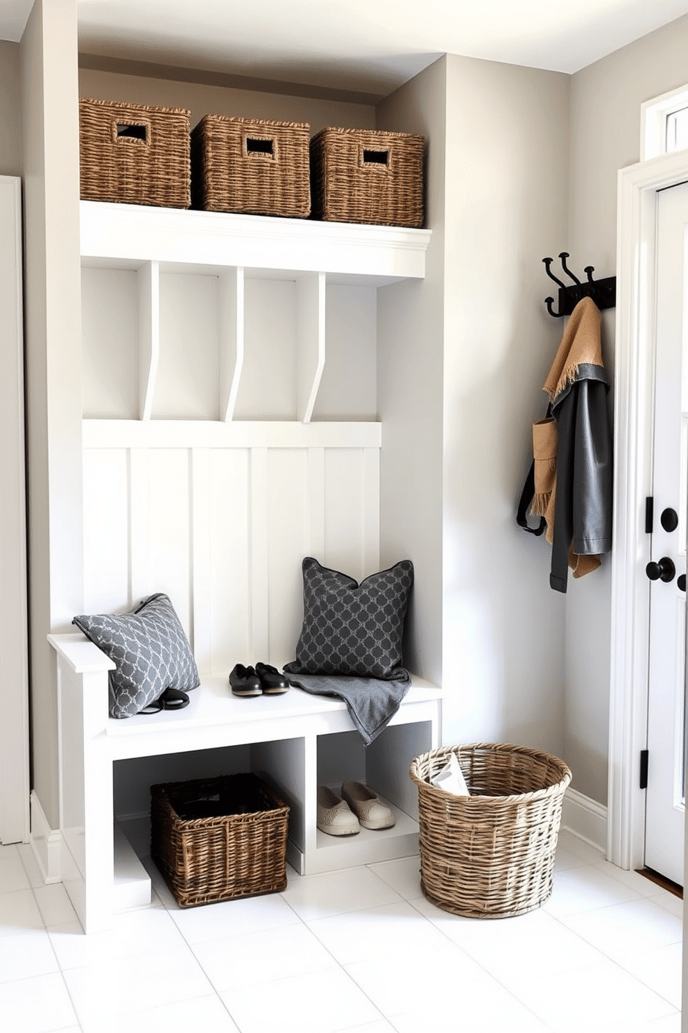 Bright white tile floor for easy cleaning. The mudroom features a built-in bench with storage cubbies above, perfect for shoes and bags. The walls are painted in a soft gray, providing a calming backdrop. A large coat rack with hooks is mounted beside the entrance, and a woven basket sits on the floor for additional organization.