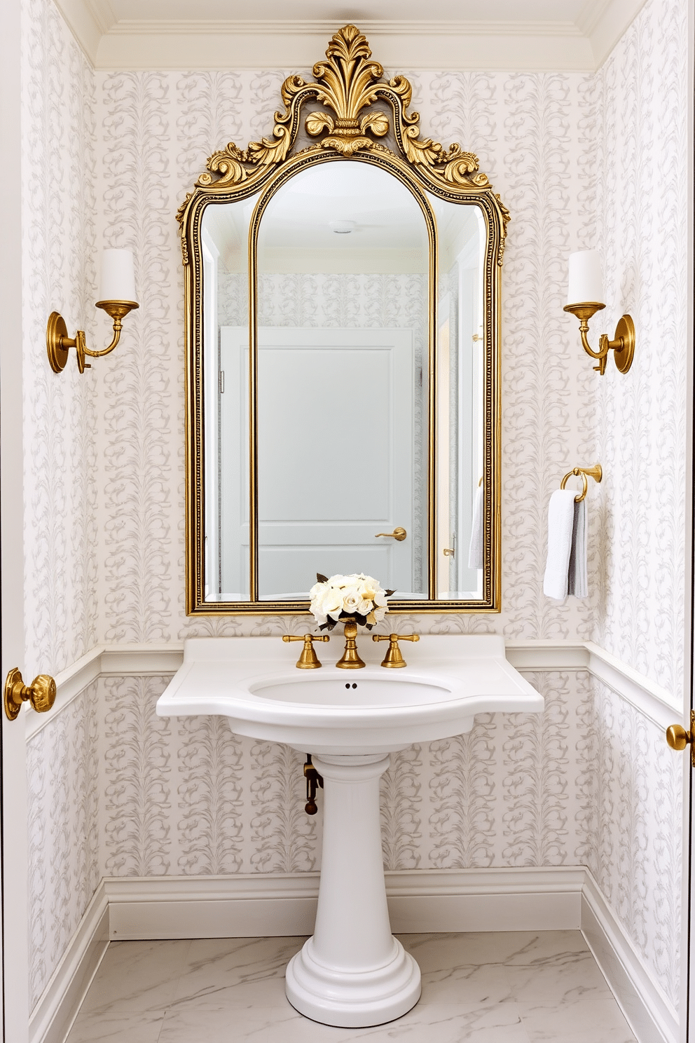 A chic powder room featuring elegant sconces flanking a large, ornate mirror. The walls are adorned with a soft white wallpaper, creating a serene backdrop for the sophisticated design elements. The floor is finished with polished white marble tiles, enhancing the room's brightness and elegance. A sleek pedestal sink sits beneath the mirror, complemented by stylish gold fixtures and a delicate floral arrangement on the countertop.