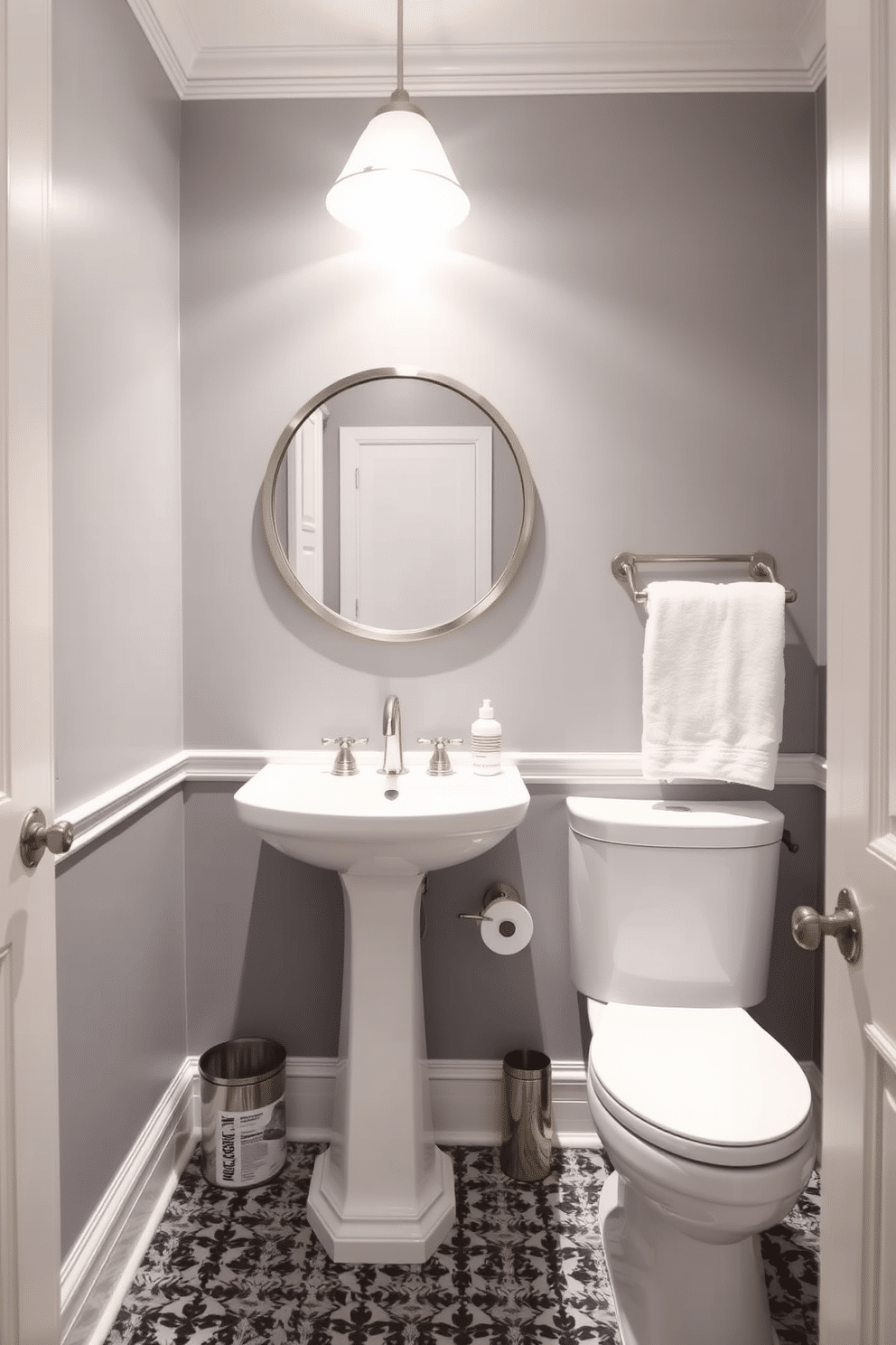 A chic powder room featuring soft gray walls complemented by elegant white trim details. The space includes a sleek pedestal sink and a round mirror framed in brushed nickel, enhancing the room's modern aesthetic.