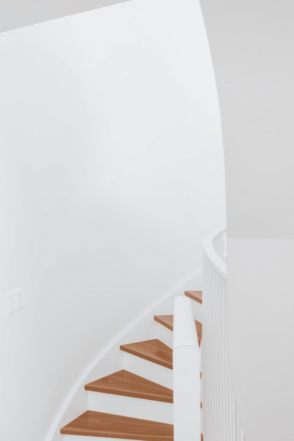 A minimalist white staircase features sleek lines and a clean aesthetic, with wooden treads that add warmth and contrast. The walls are painted in a crisp white, enhancing the airy feel, while a simple railing complements the overall design without overpowering it.