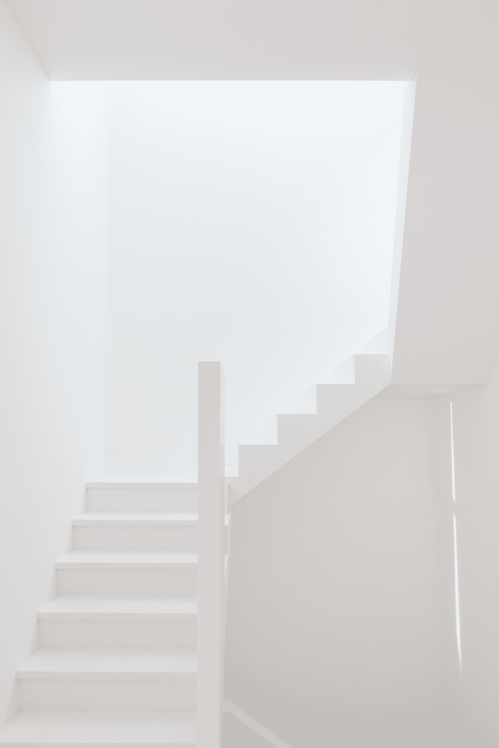 A sleek, white staircase with a minimalist aesthetic features clean lines and a floating design that maximizes light and space. The surrounding walls are painted in a soft, neutral tone, creating a serene backdrop that enhances the staircase's modern appeal.