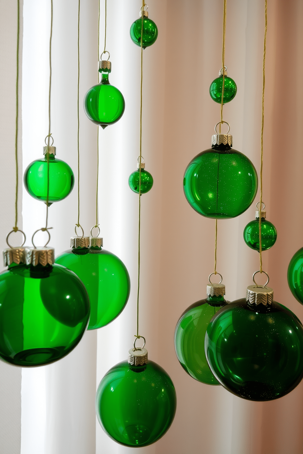 A festive St. Patrick's Day display featuring hanging green glass ornaments in various shapes and sizes. The ornaments shimmer in the light, suspended from delicate gold threads against a backdrop of soft white curtains.