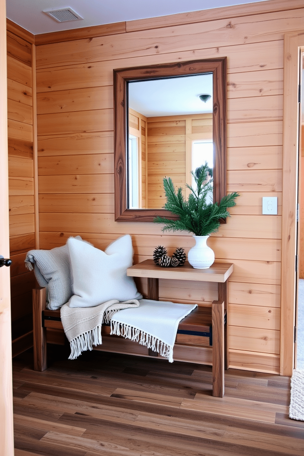 A cozy winter entryway features natural wood accents that create a warm and inviting atmosphere. A rustic wooden bench is placed against the wall, adorned with plush throw pillows and a soft blanket for added comfort. The walls are lined with wooden paneling, enhancing the natural aesthetic while providing a sense of warmth. A large, framed mirror with a wooden frame hangs above a small console table, which displays seasonal decorations like pinecones and evergreen branches.